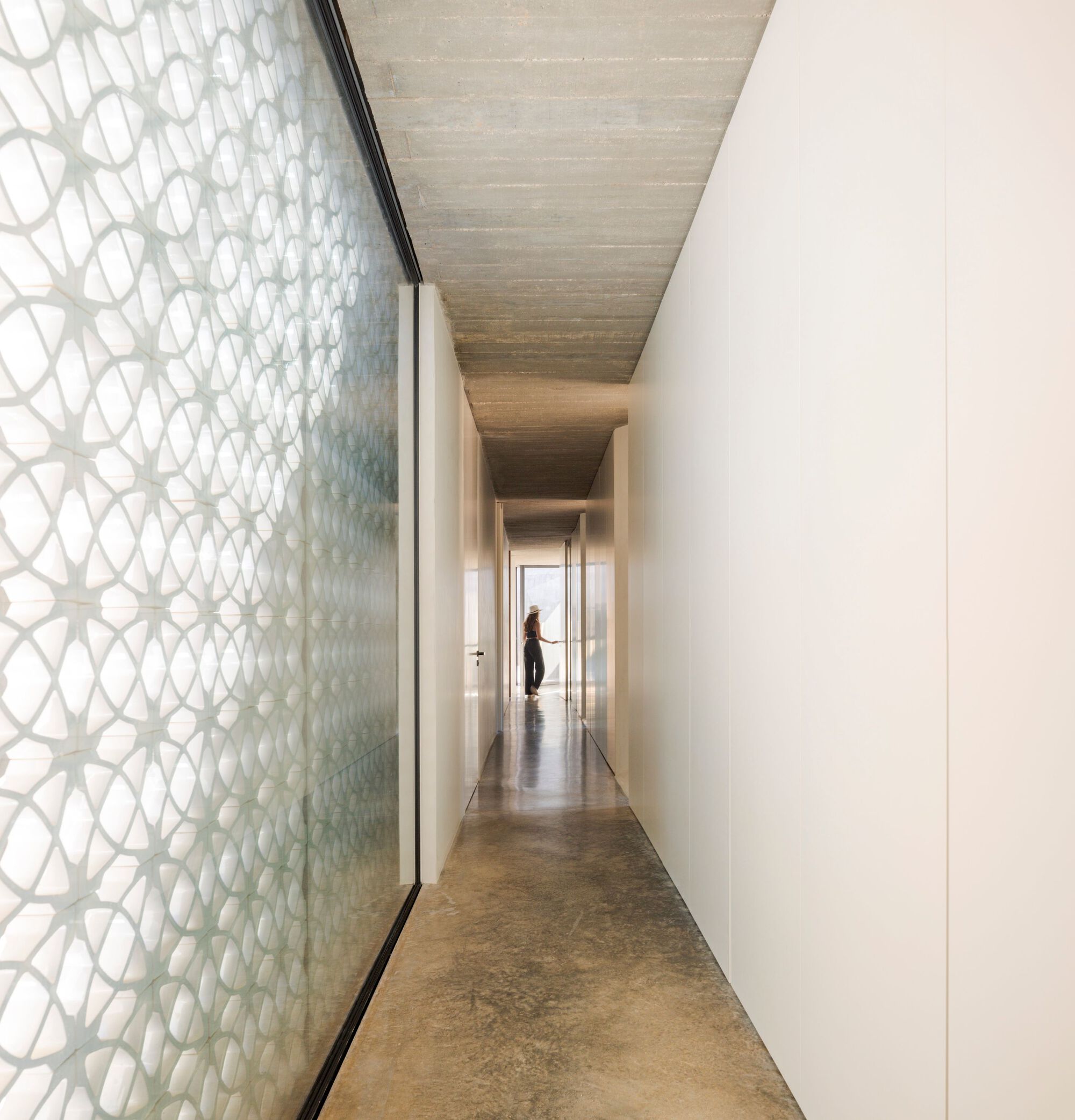 Corridor with patterned glass screen wall and timber ceiling viewed toward a figure in daylight