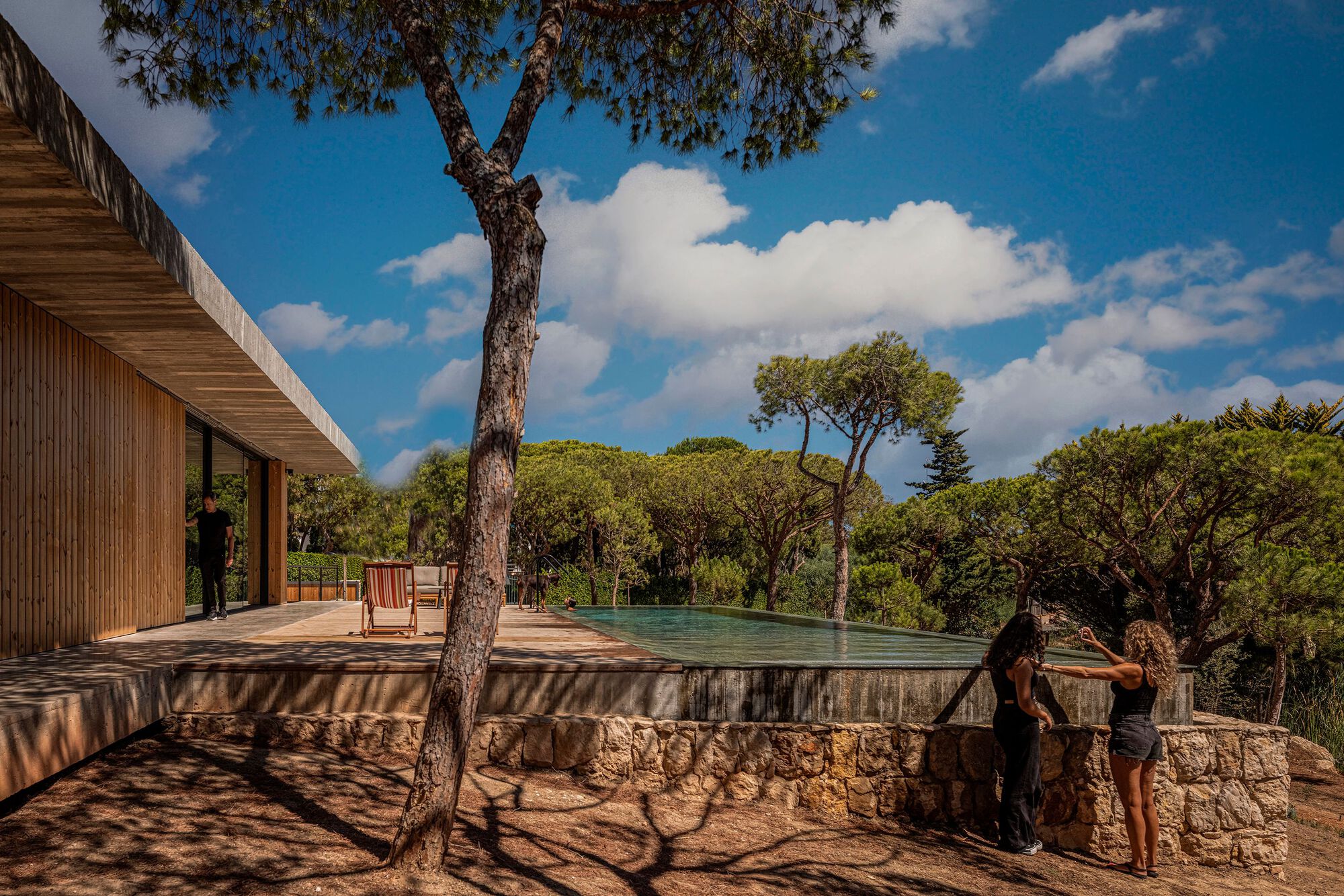 Raised pool terrace with stone wall base and two figures silhouetted against the tree canopy