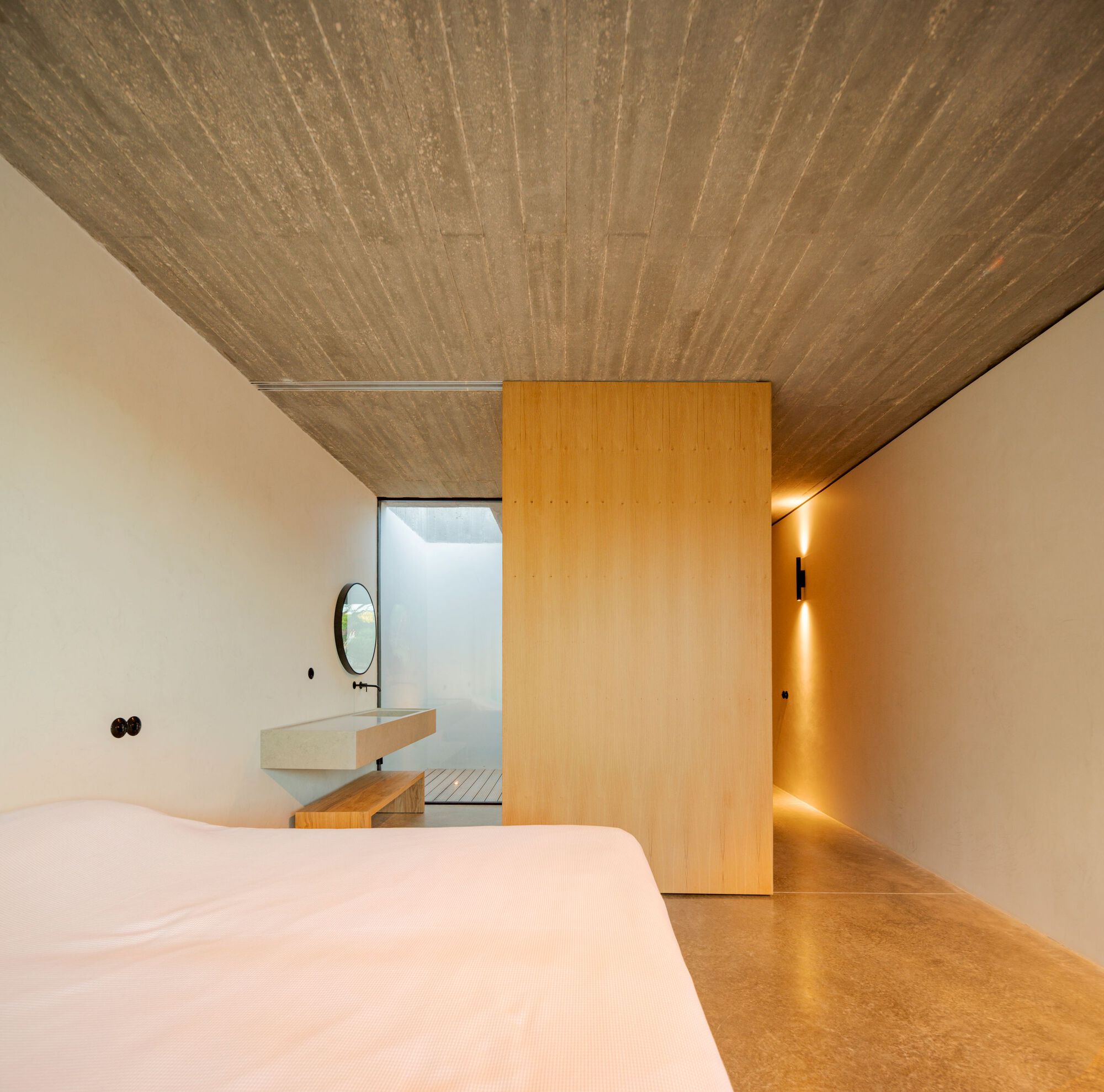 Bedroom with board-formed concrete ceiling and sliding timber door revealing ensuite bathroom