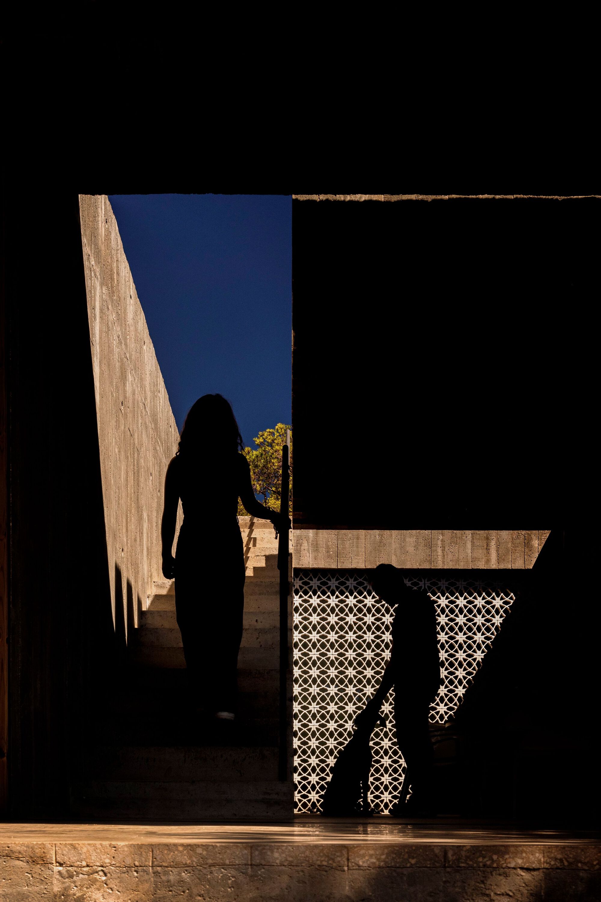 Silhouetted figure in doorway framing view of concrete volumes and patterned screen under deep blue twilight sky
