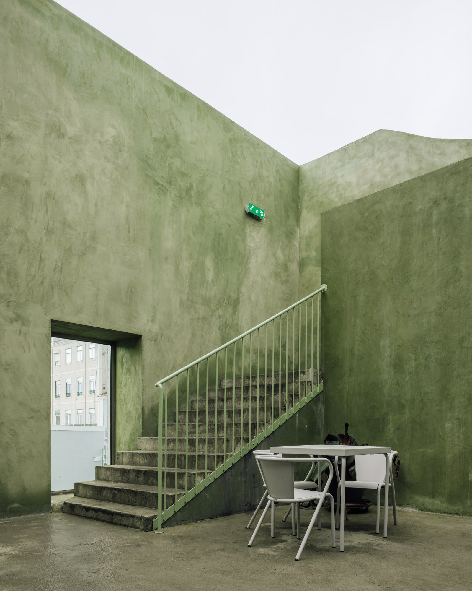 Interior staircase with metal balustrade in a space with pale green polished plaster walls and a table below