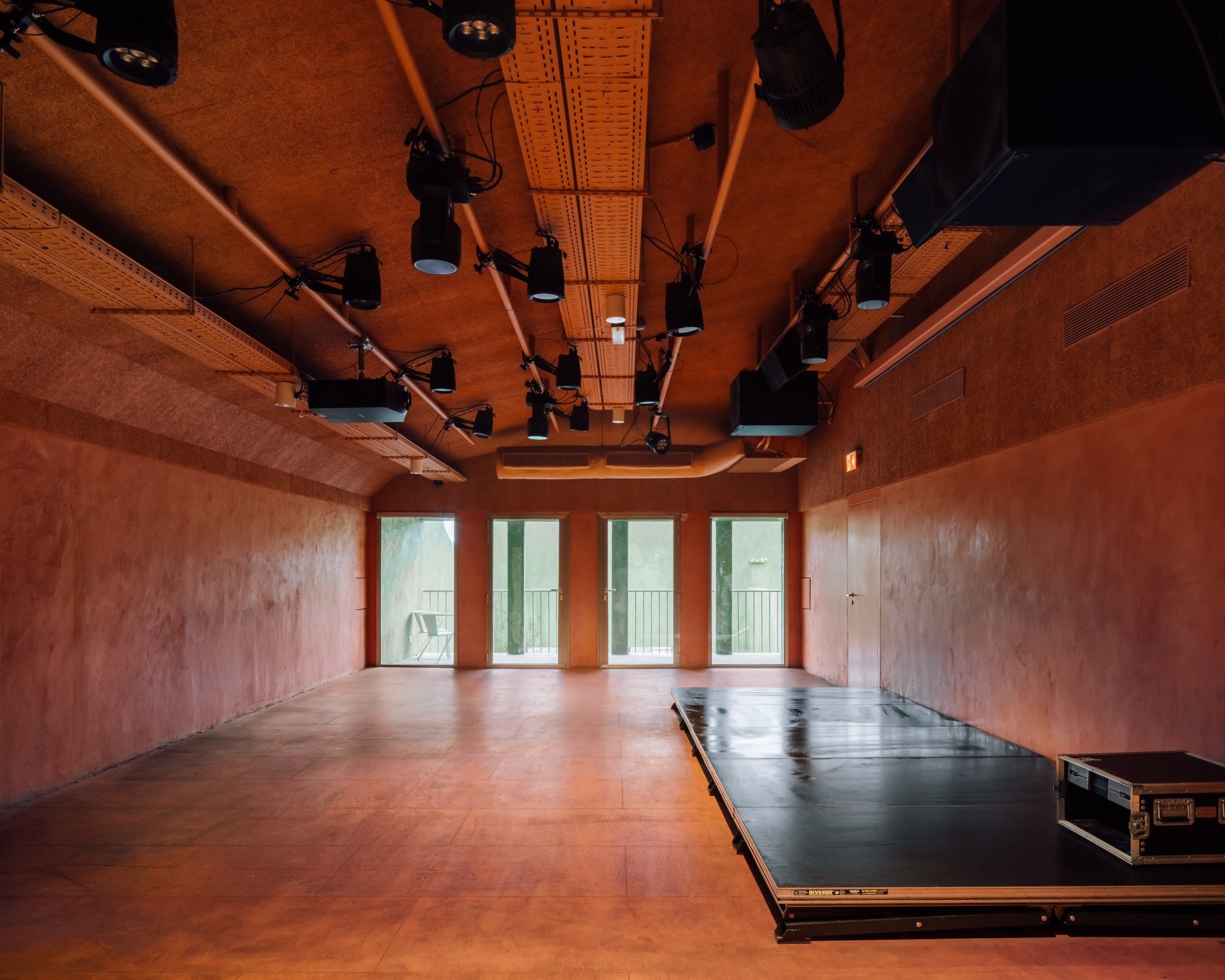 Performance room with terracotta plaster walls, timber ceiling, and retractable stage platform under theatrical lighting