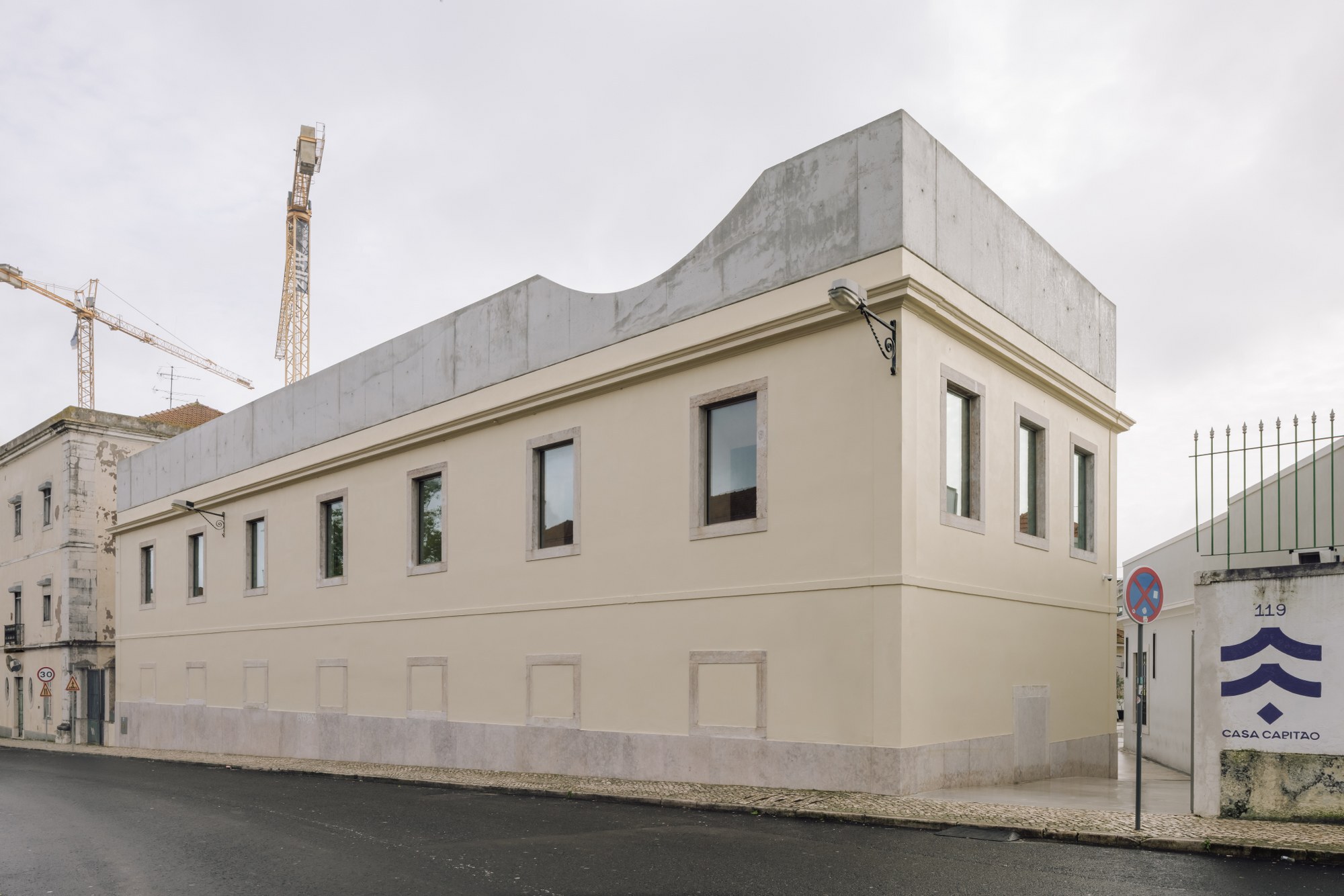 Street corner view showing cream facade with concrete volume above and construction cranes in background