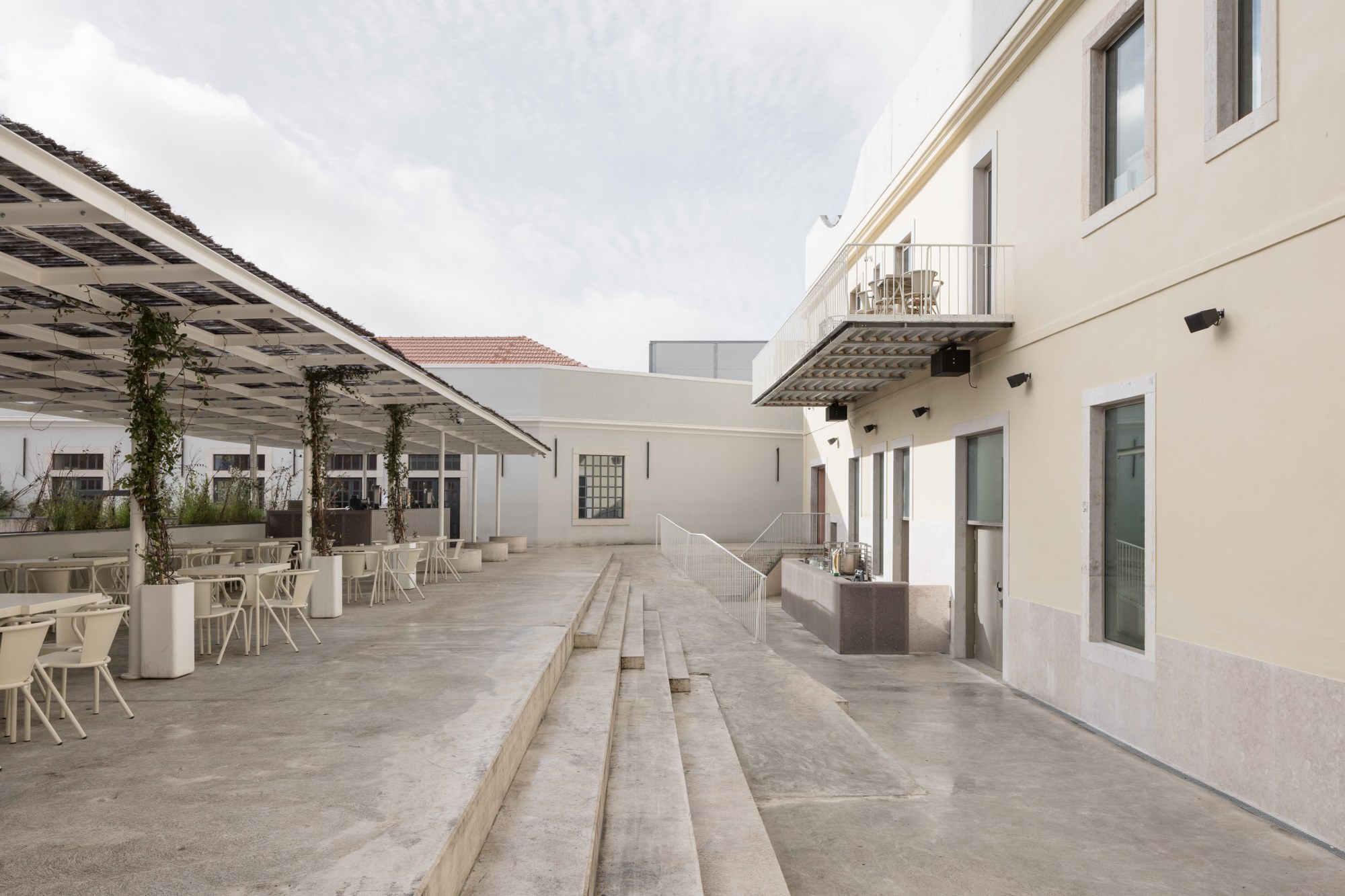 Courtyard with concrete stepped seating, canopy-covered terrace, and planters with climbing vegetation