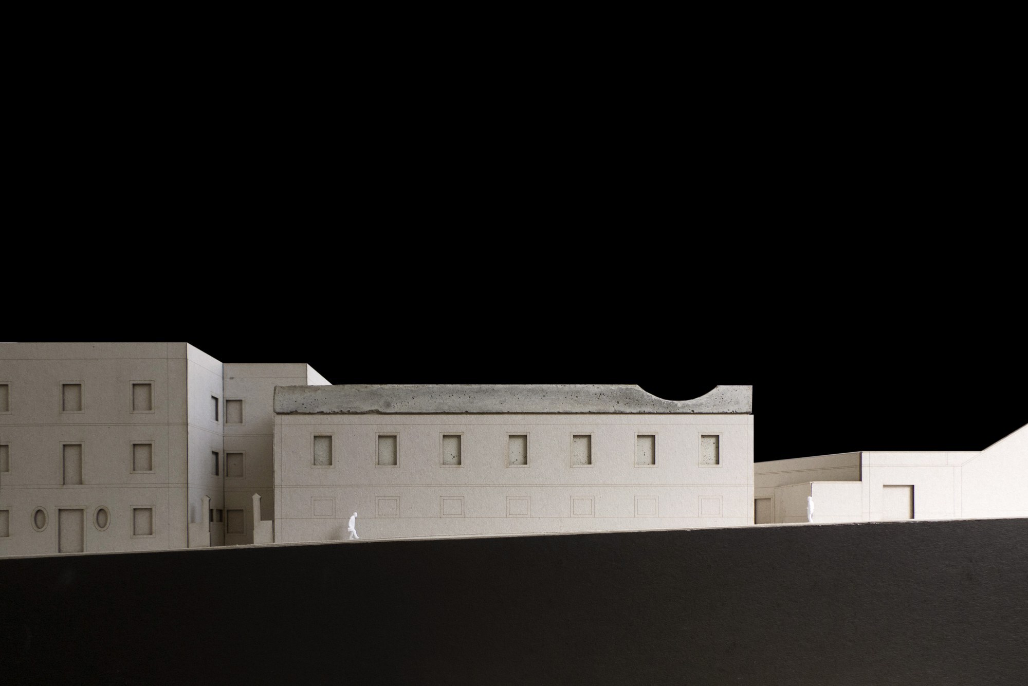 Sectional model showing a long rectangular facade with punched windows and a single figure on the ground plane