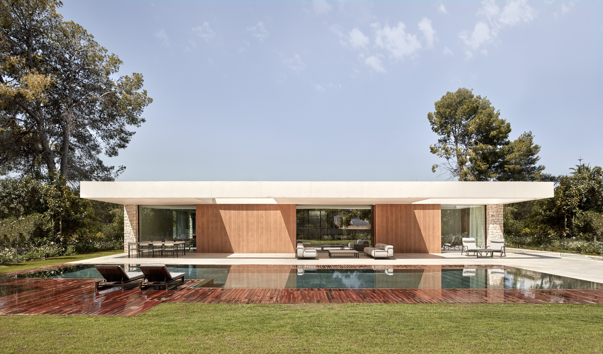 Garden facade with flat roof and wood-clad volumes flanking a covered terrace overlooking the swimming pool