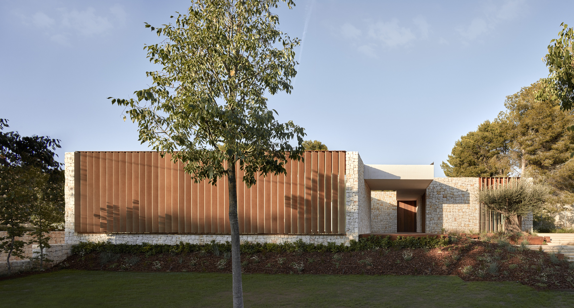 Street view showing vertical timber screen and stone plinth base with trees emerging from planted beds