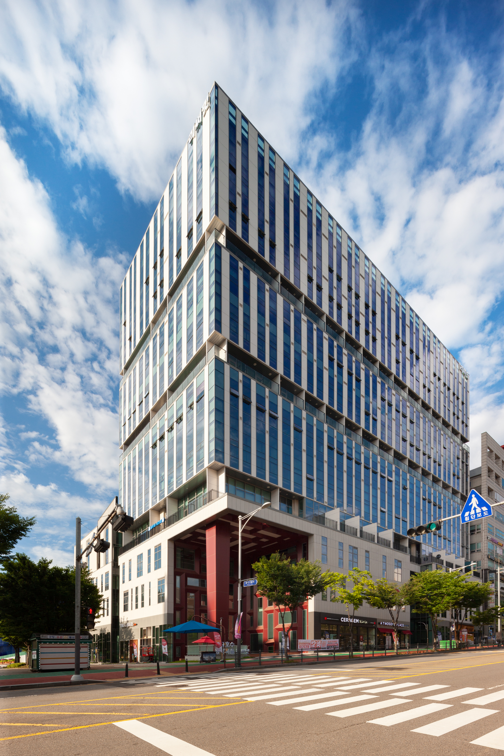 Street corner view of the vertically striped facade with cantilevered floor plates under scattered clouds