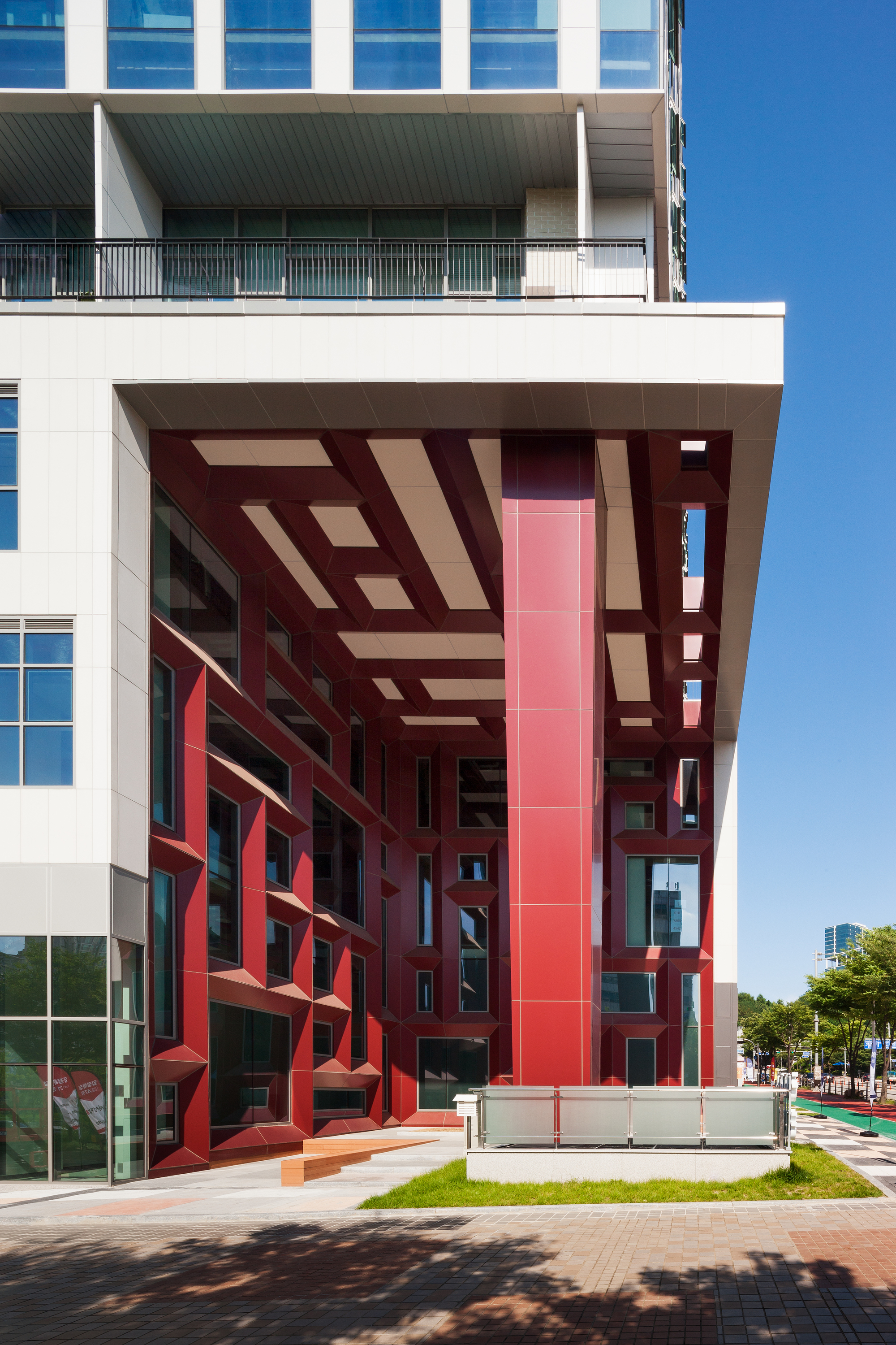 Red geometric metal framework wrapping the ground-level entry canopy beside a glazed lobby