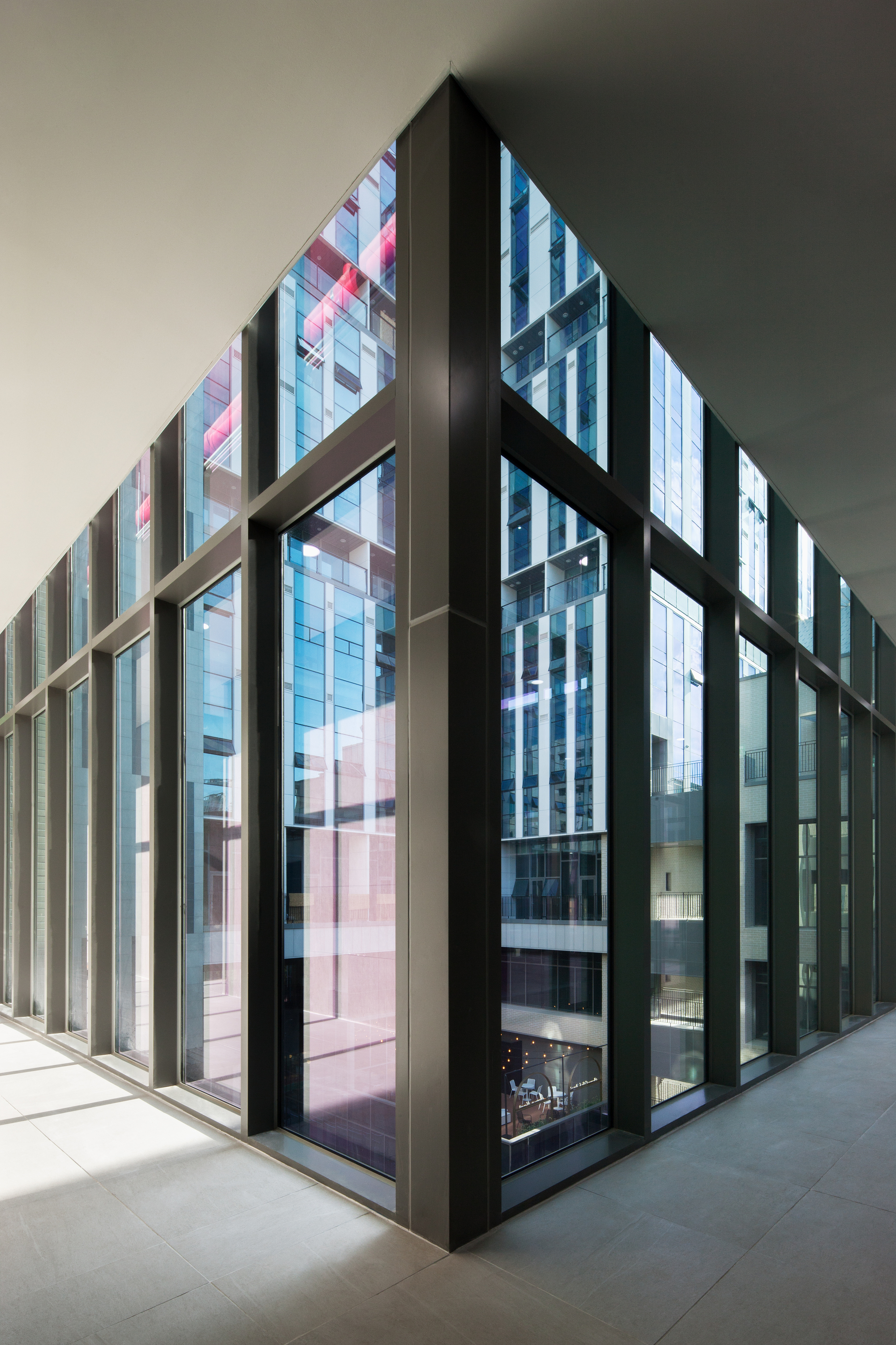 Corner interior corridor with floor-to-ceiling glass walls in dark metal frames reflecting pink and blue panels