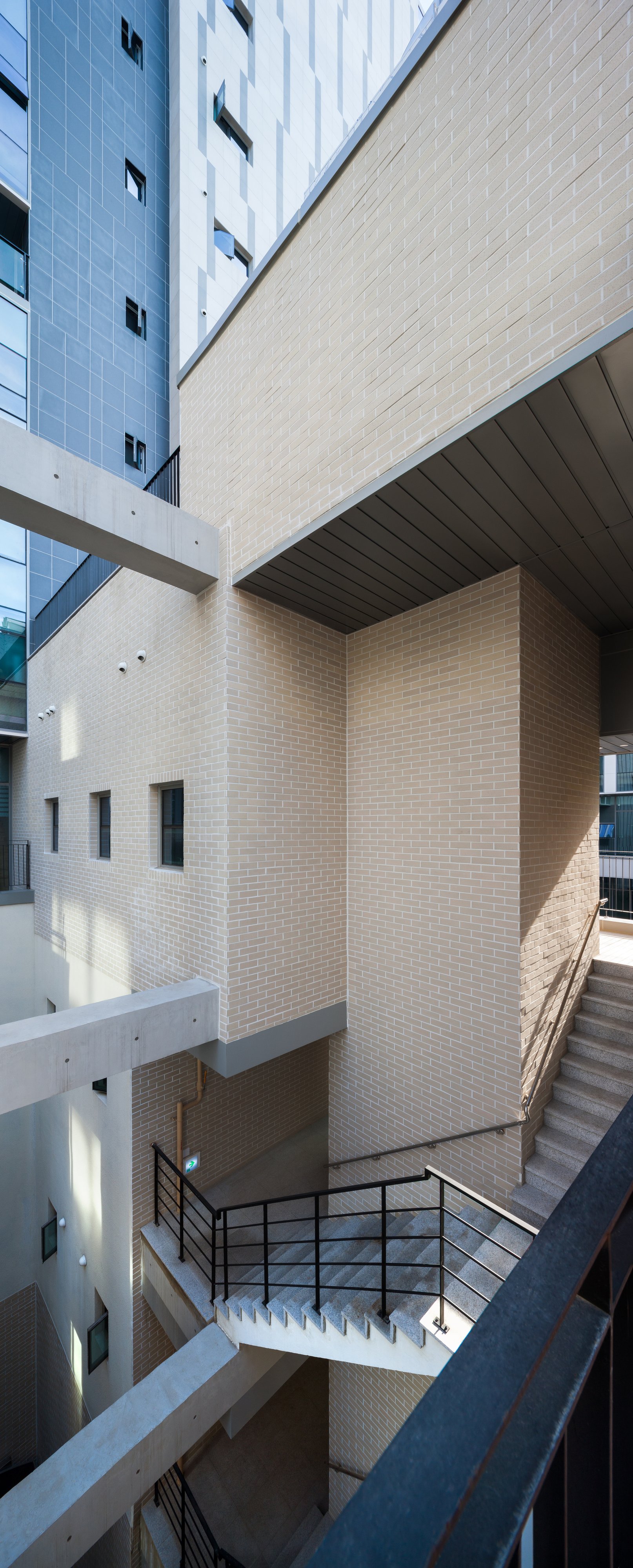 Multi-level atrium with pale brick walls, cantilevered volumes, and metal stair railings in bright daylight