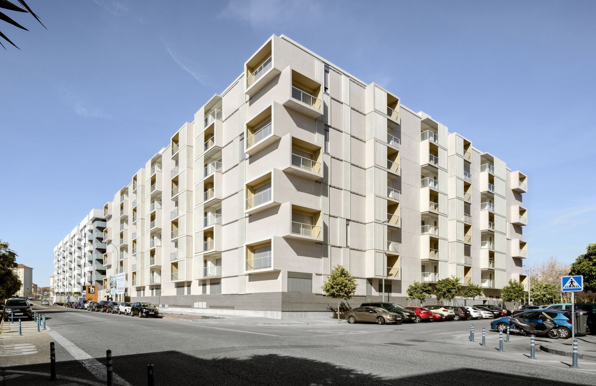 Street corner view of the white paneled residential block with recessed balconies under clear blue sky