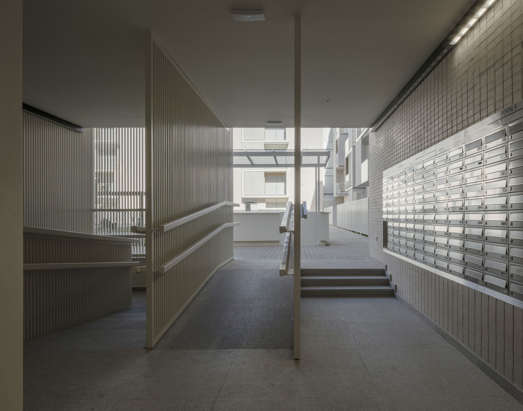 Ground floor lobby with metal mailboxes, ribbed wall panels and steps leading to glazed courtyard