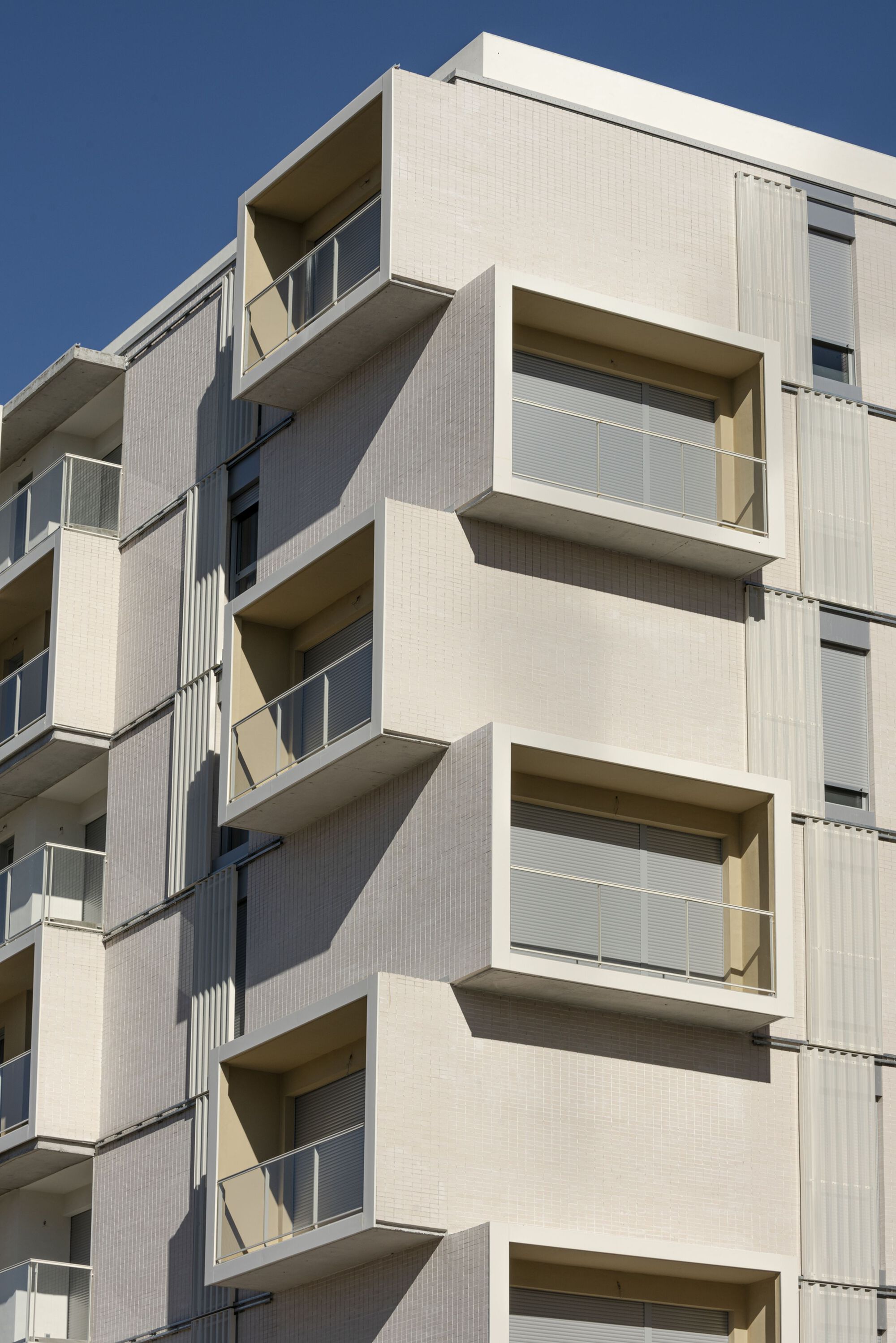 Close-up of stacked balconies with glass railings and white ribbed cladding in afternoon sunlight