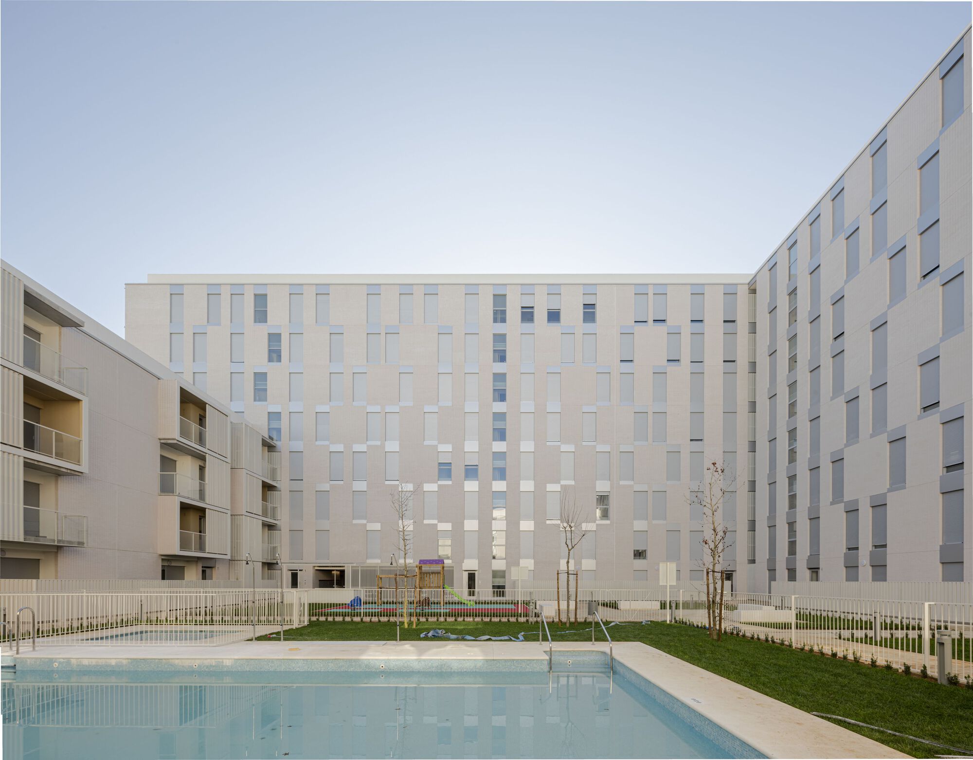 Courtyard view showing chequered facade panels, a reflecting pool, and newly planted trees