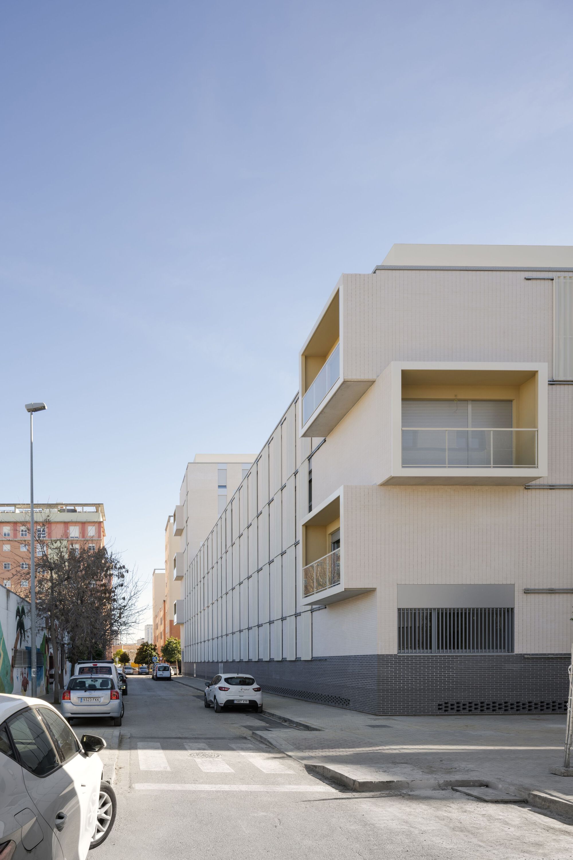 Corner view showing projecting balconies with yellow reveals and the metal panel facade in afternoon light