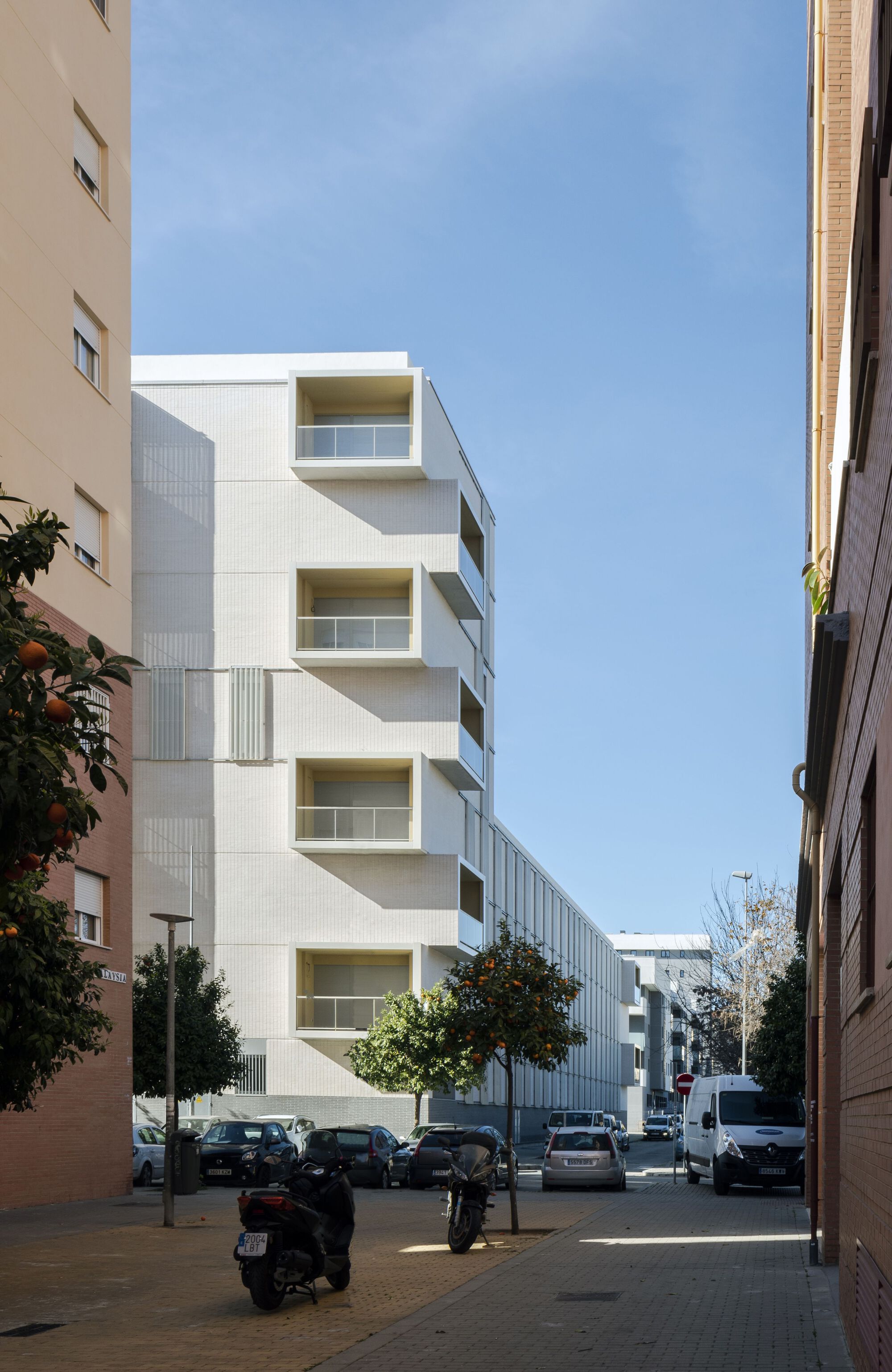 Street view through neighboring buildings showing the white facade with cantilevered balconies and street trees