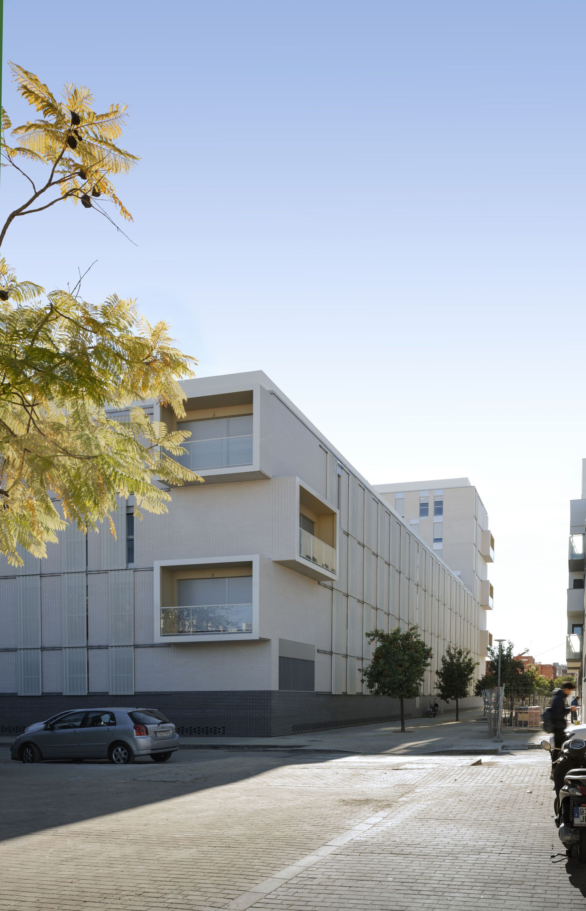 Street view of the white paneled facade with projecting balconies and a tree in the foreground