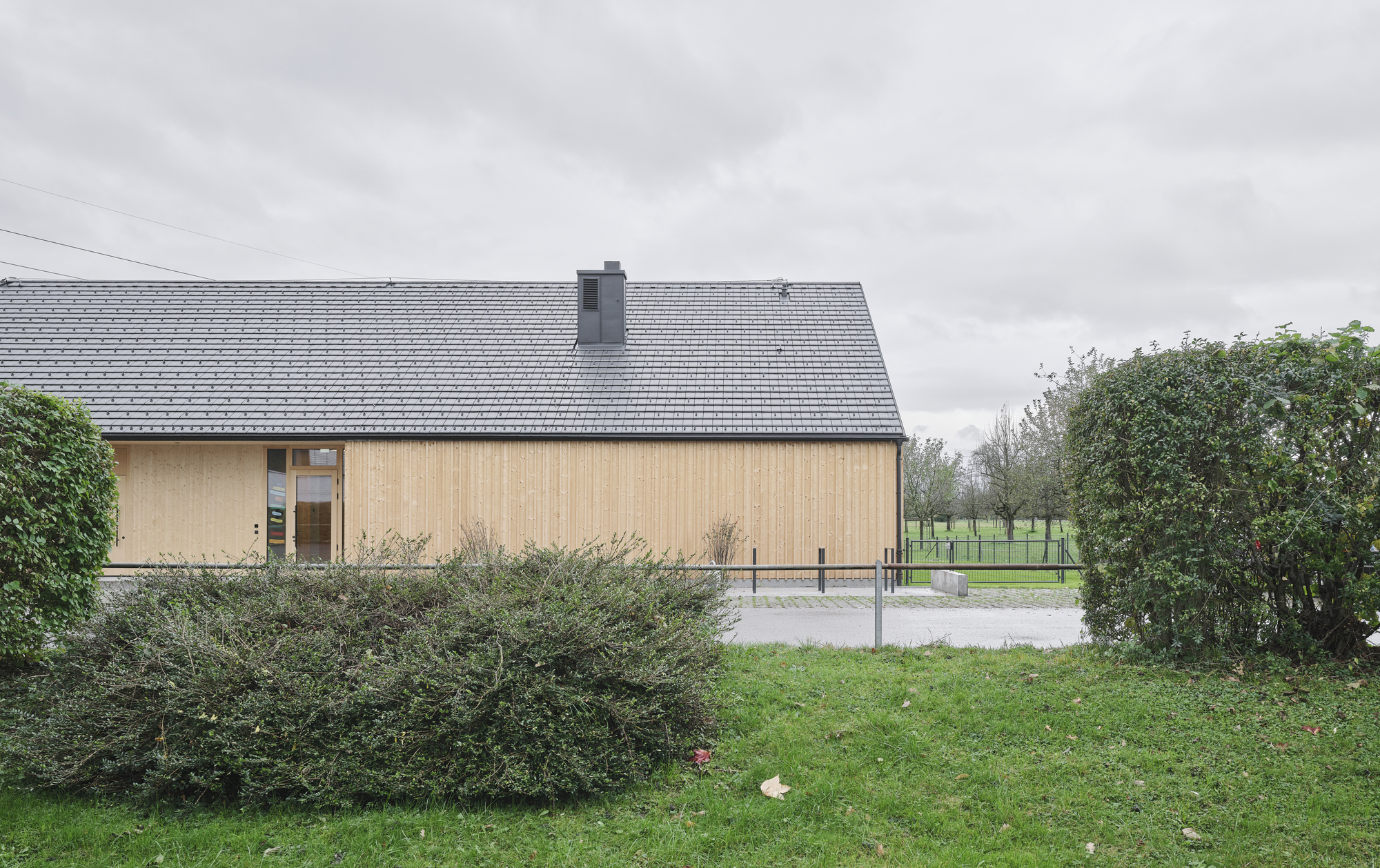 Gable end elevation with vertical timber cladding and small entrance portal beside low shrubs