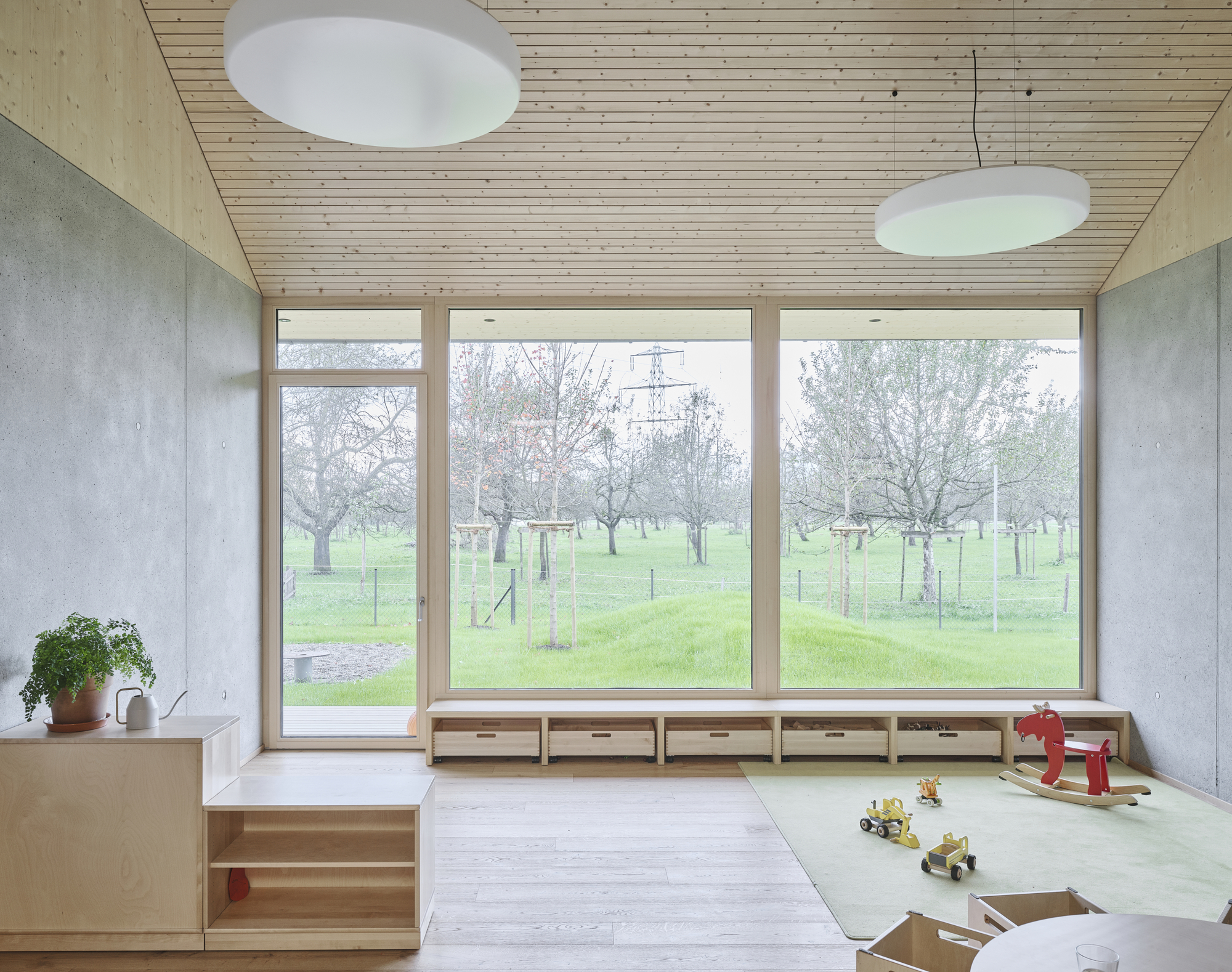 Interior room with timber ceiling, concrete walls, low built-in storage and windows overlooking park
