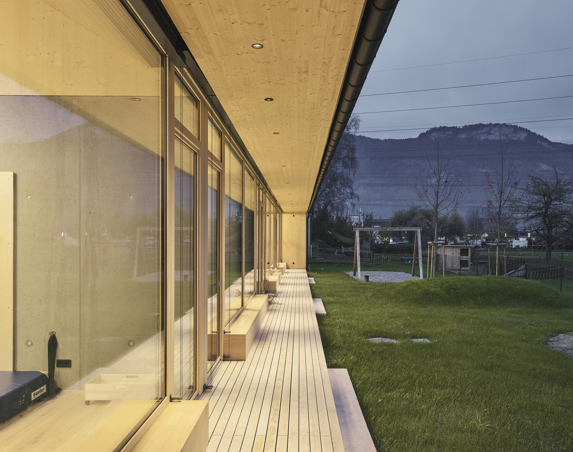 Long exterior deck alongside glazed facade with hills visible beyond the grassy field