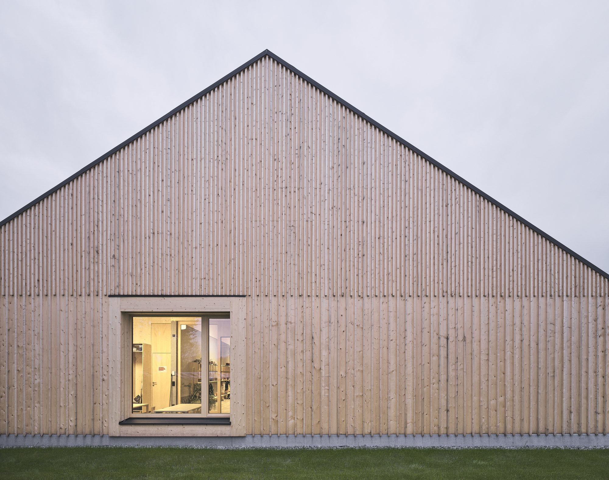 Vertical timber slat gable facade with single punched window opening at twilight