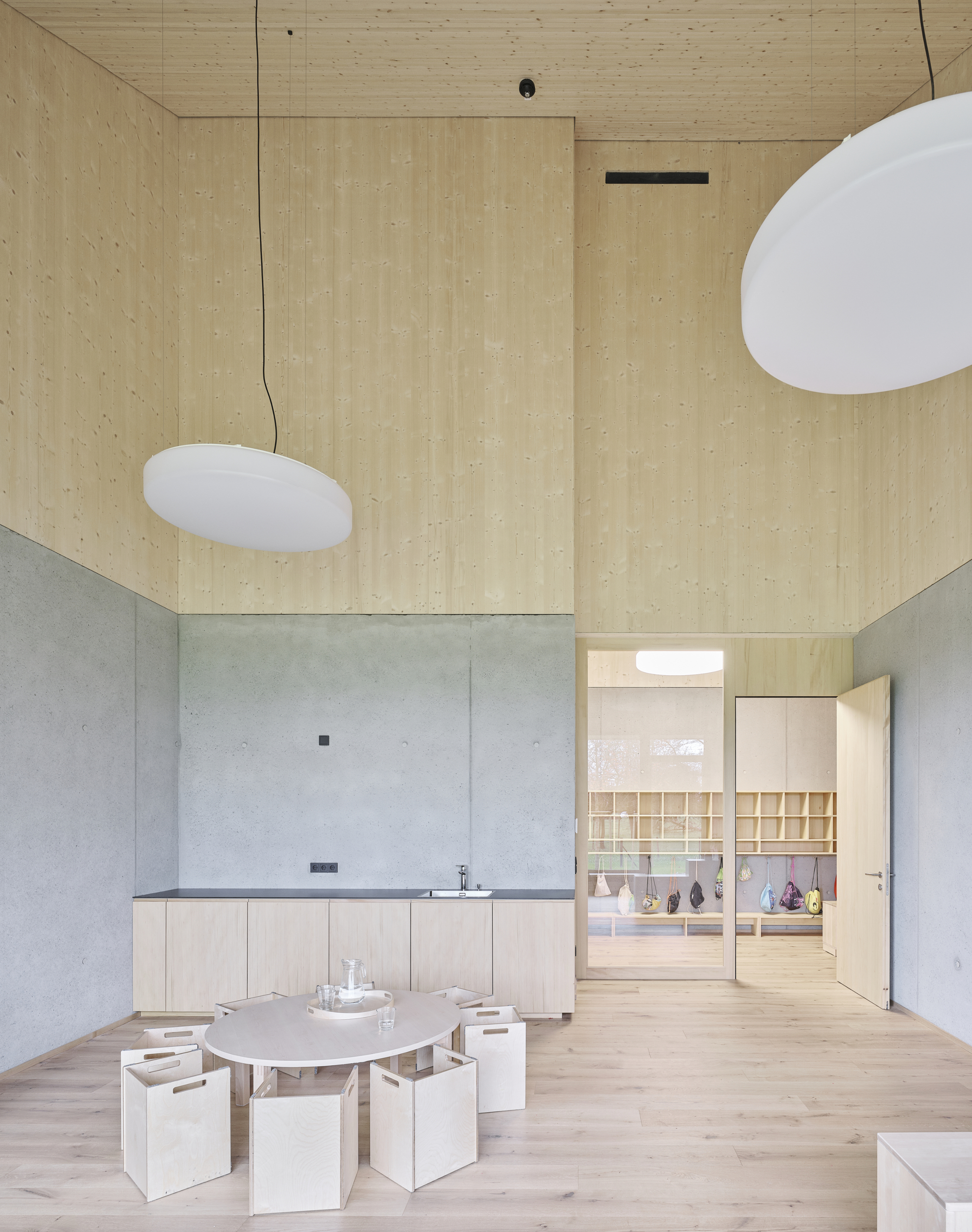 Double-height interior with plywood walls and ceiling above a concrete base and low seating around a table