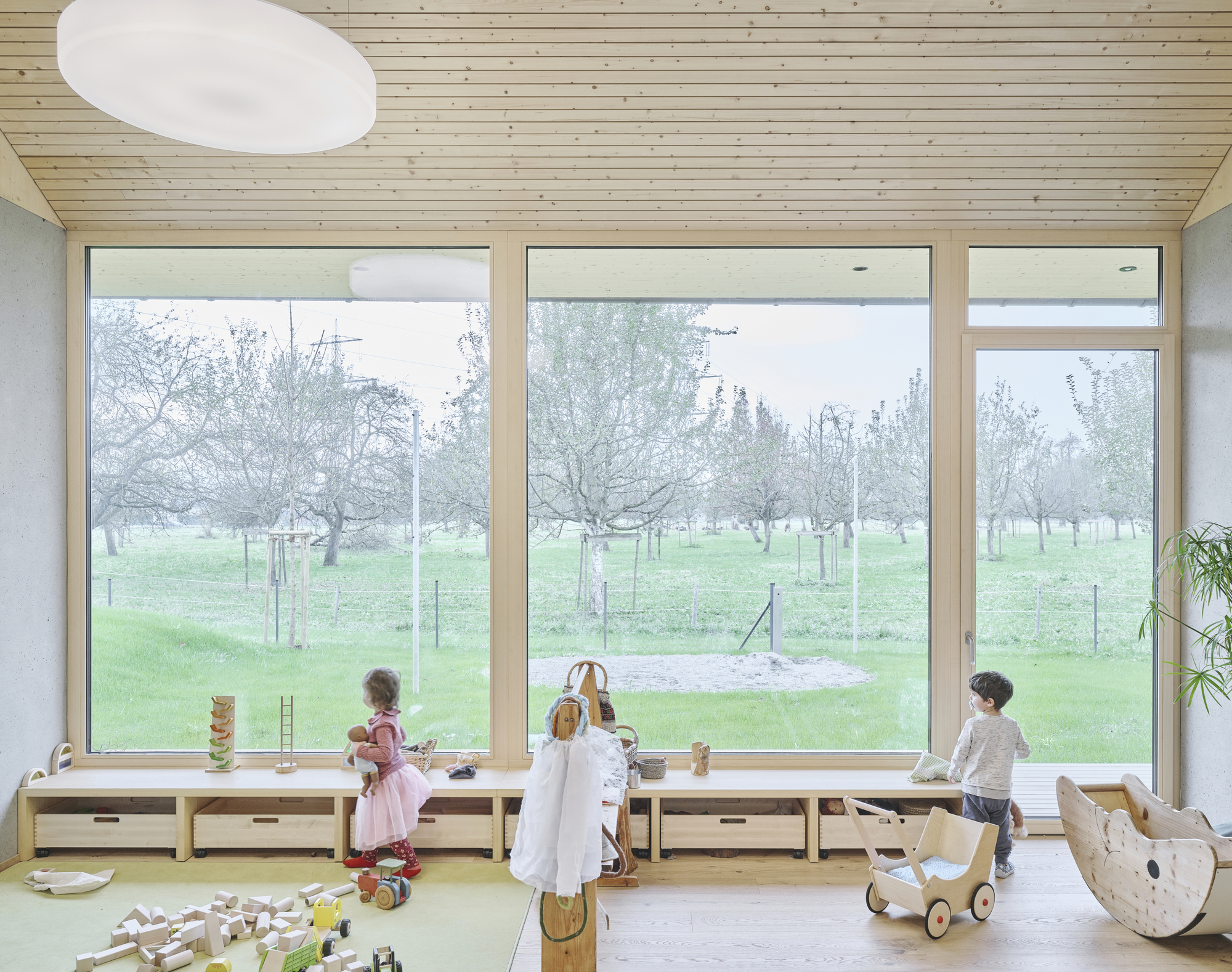Children playing in a room with floor-to-ceiling windows overlooking the orchard on a misty morning