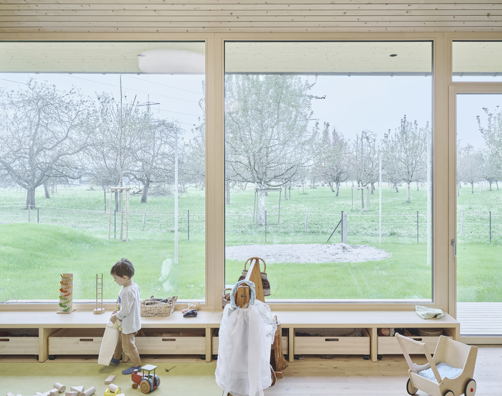 Two children at the window bench with wooden toys looking out to the fenced pasture and trees