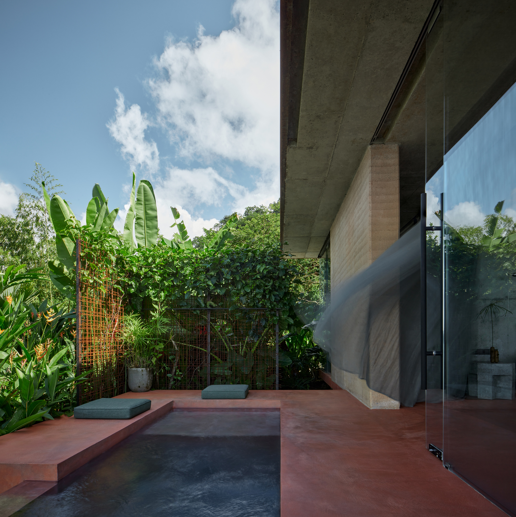 Red-tinted terrace with plunge pool bordered by banana plants and tropical foliage under bright sun