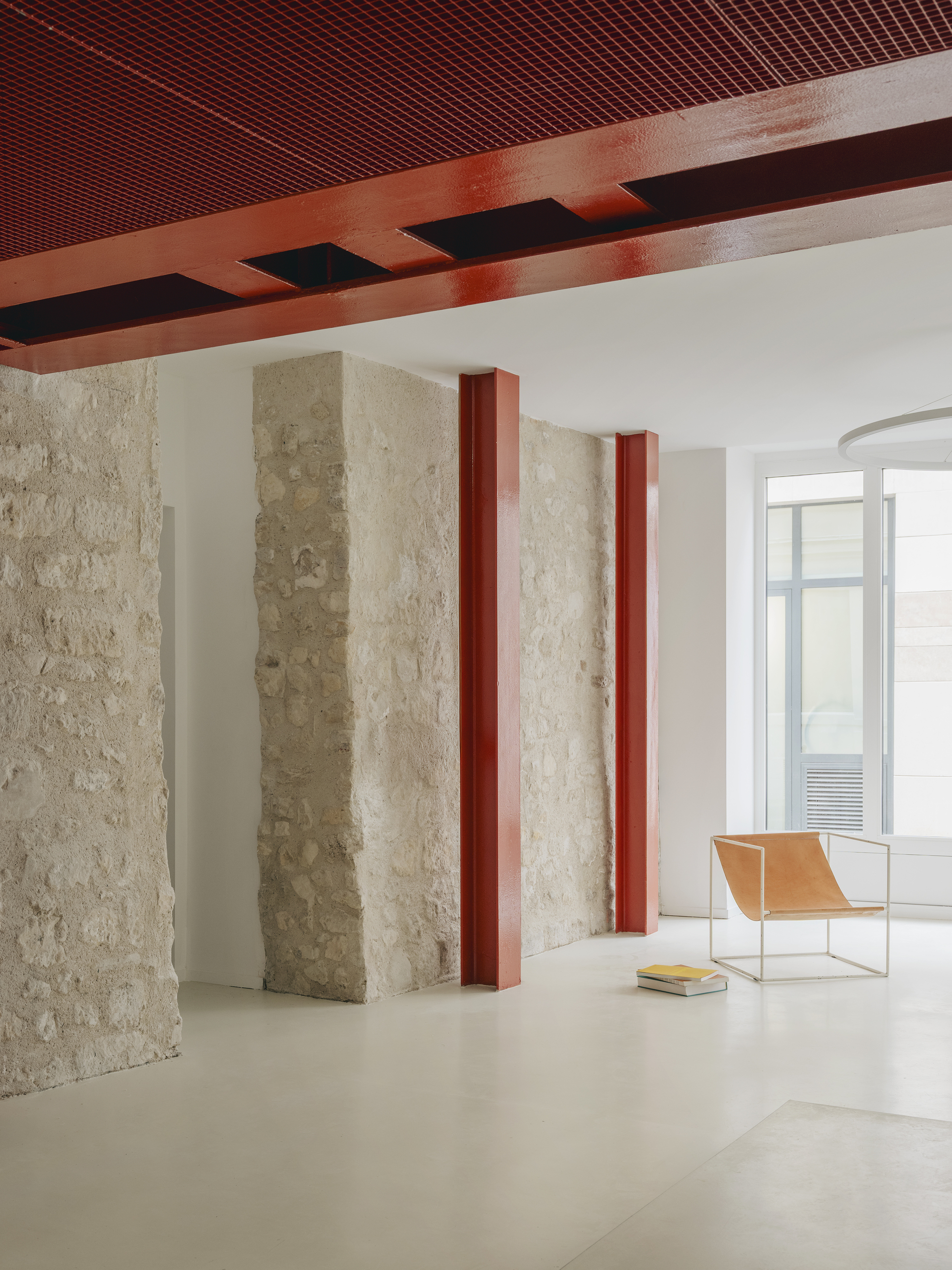 Interior with retained stone walls framed by red steel columns beneath a perforated metal ceiling