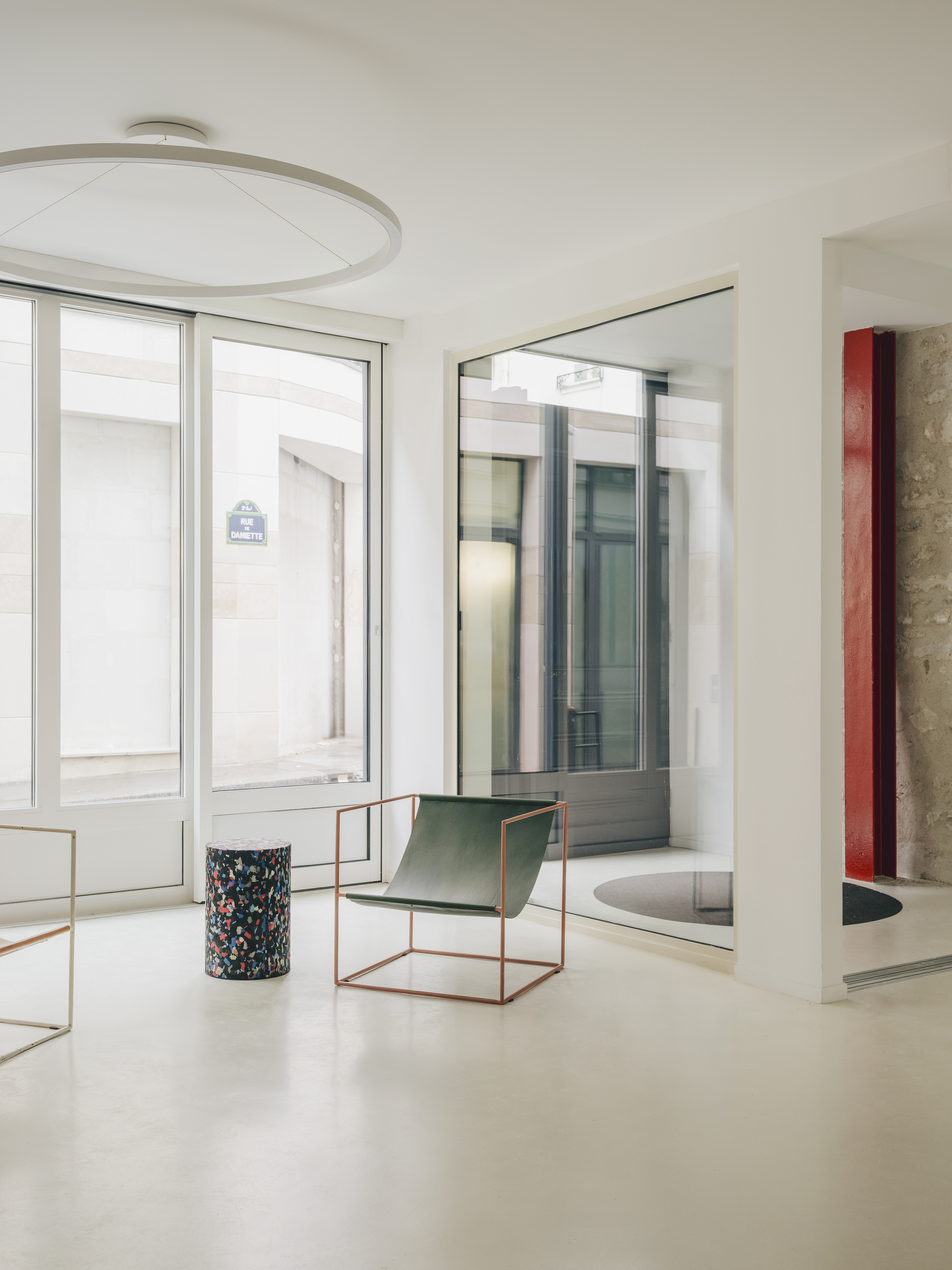 White interior with brass-framed seating and terrazzo planter beneath a circular ceiling fixture