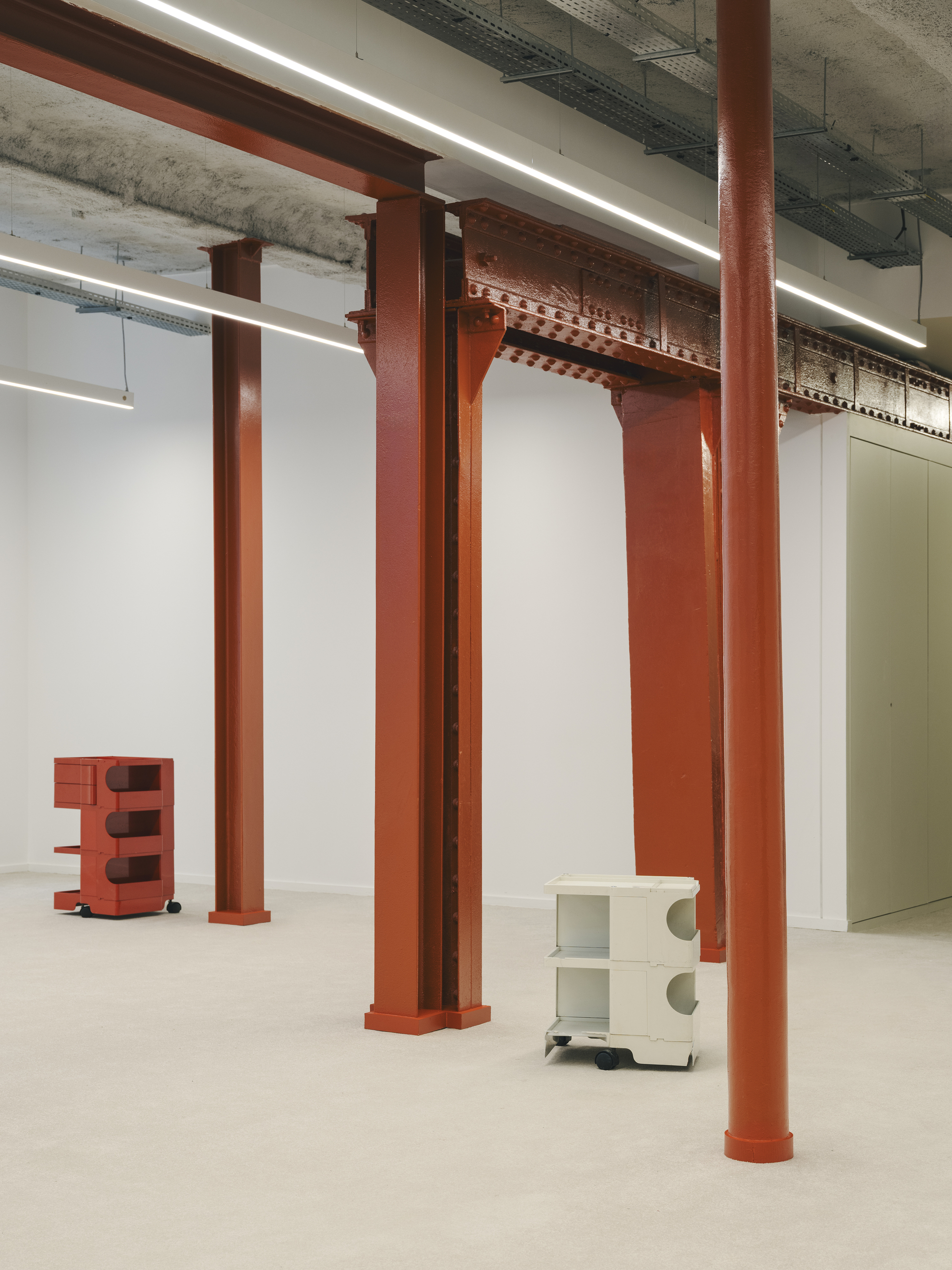 Close view of orange steel columns with decorative capitals beneath exposed concrete structure and services