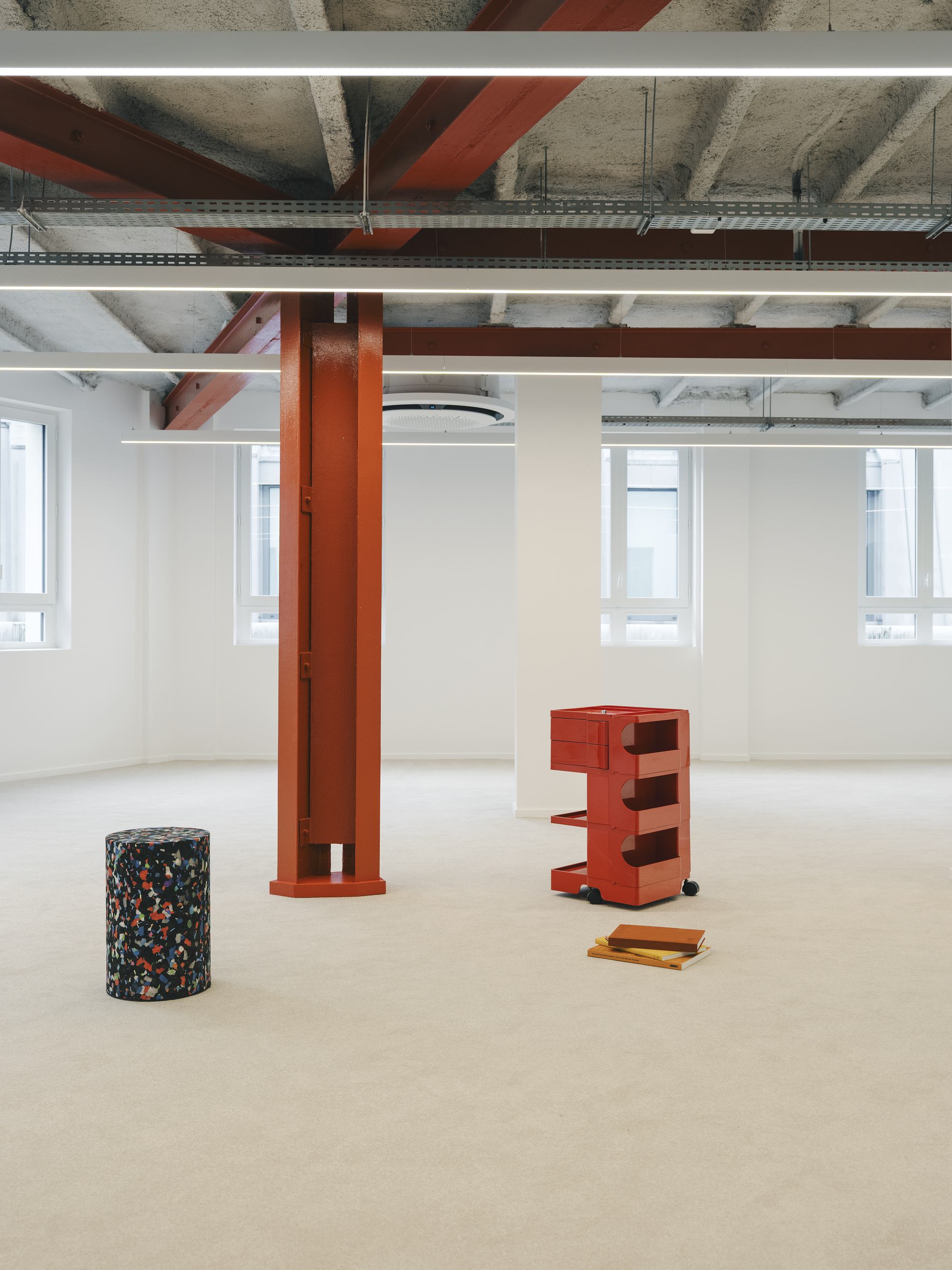 Open floor with orange column, terrazzo cylinder and wheeled storage unit beneath exposed structure