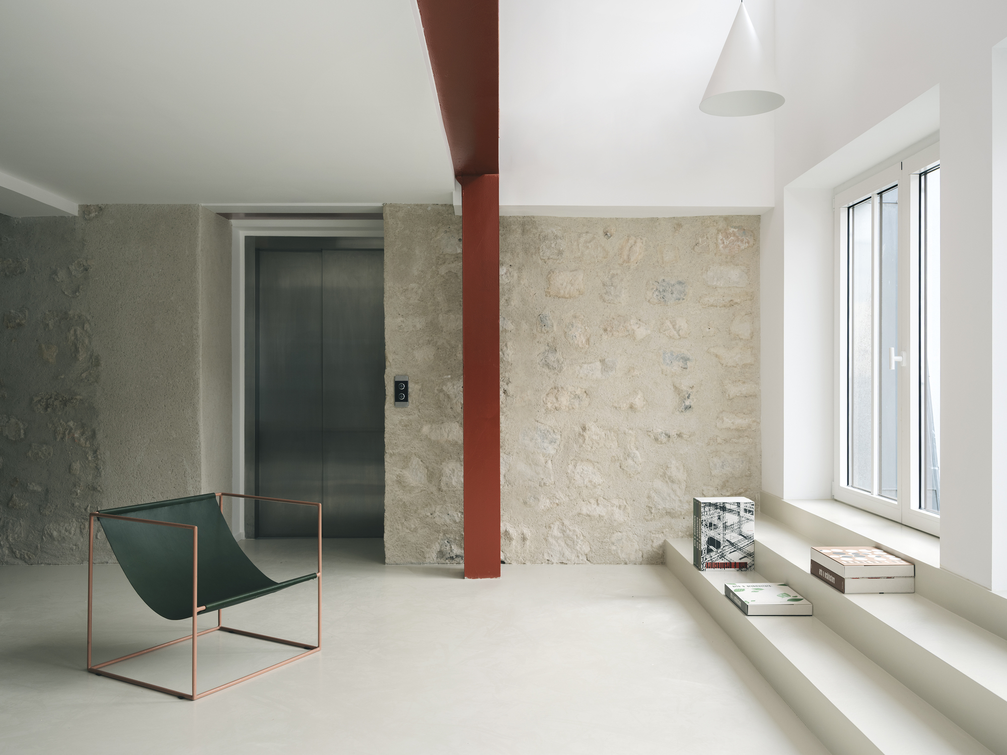 Room with textured limestone walls, a red steel column, and a metal sling chair beside a window