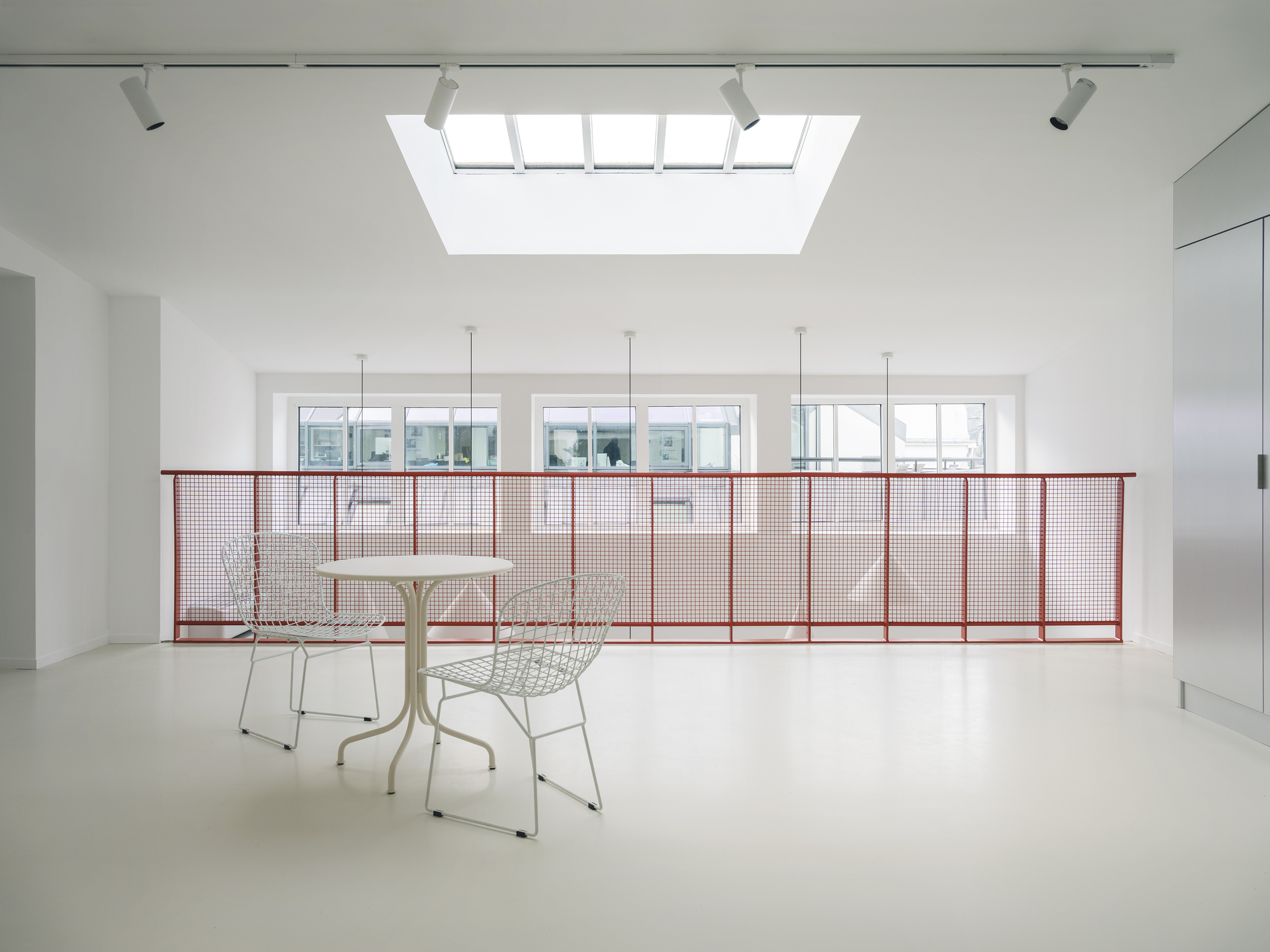 Upper level with red mesh railing and central skylight illuminating the white interior space