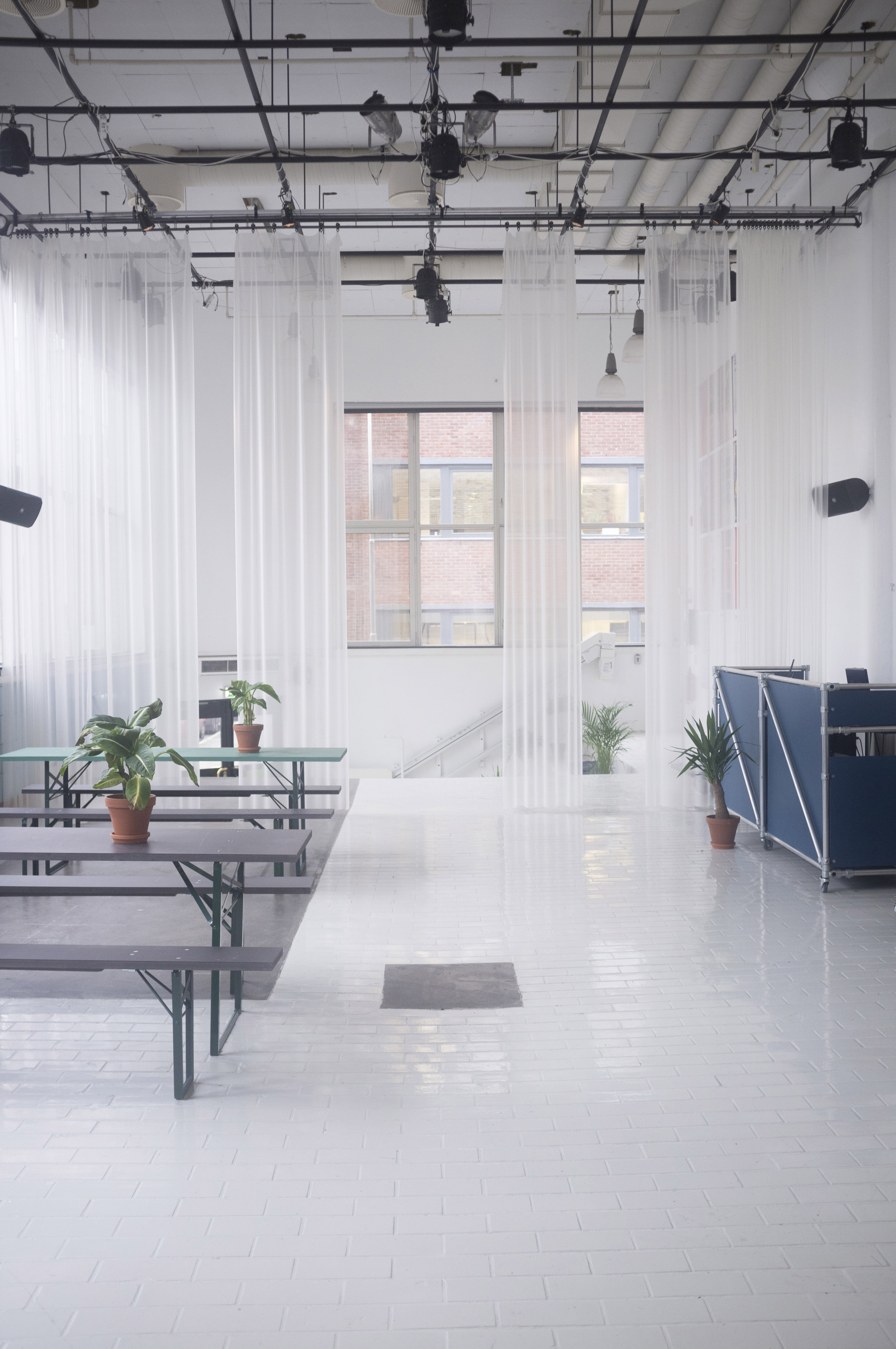 Folding bench tables on white tile flooring beneath windows overlooking adjacent brick buildings