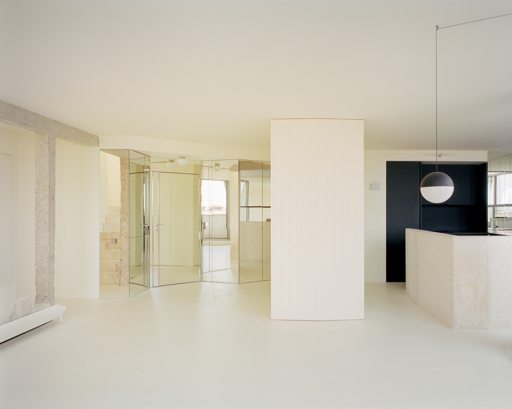 Open plan living area with fluted white volume, mirrored partition and black kitchen beyond