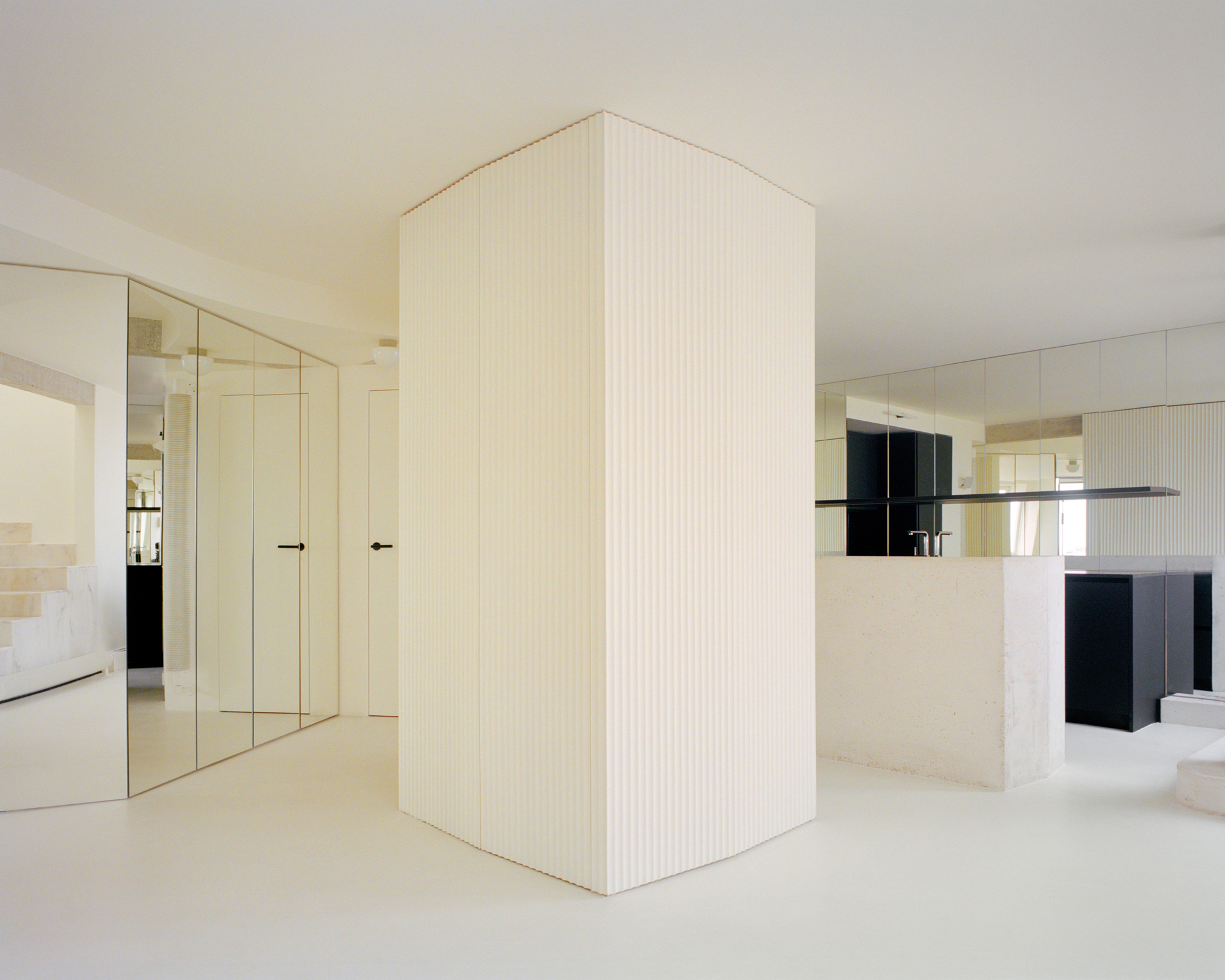 Freestanding fluted enclosure anchoring the space between mirrored doors and kitchen island