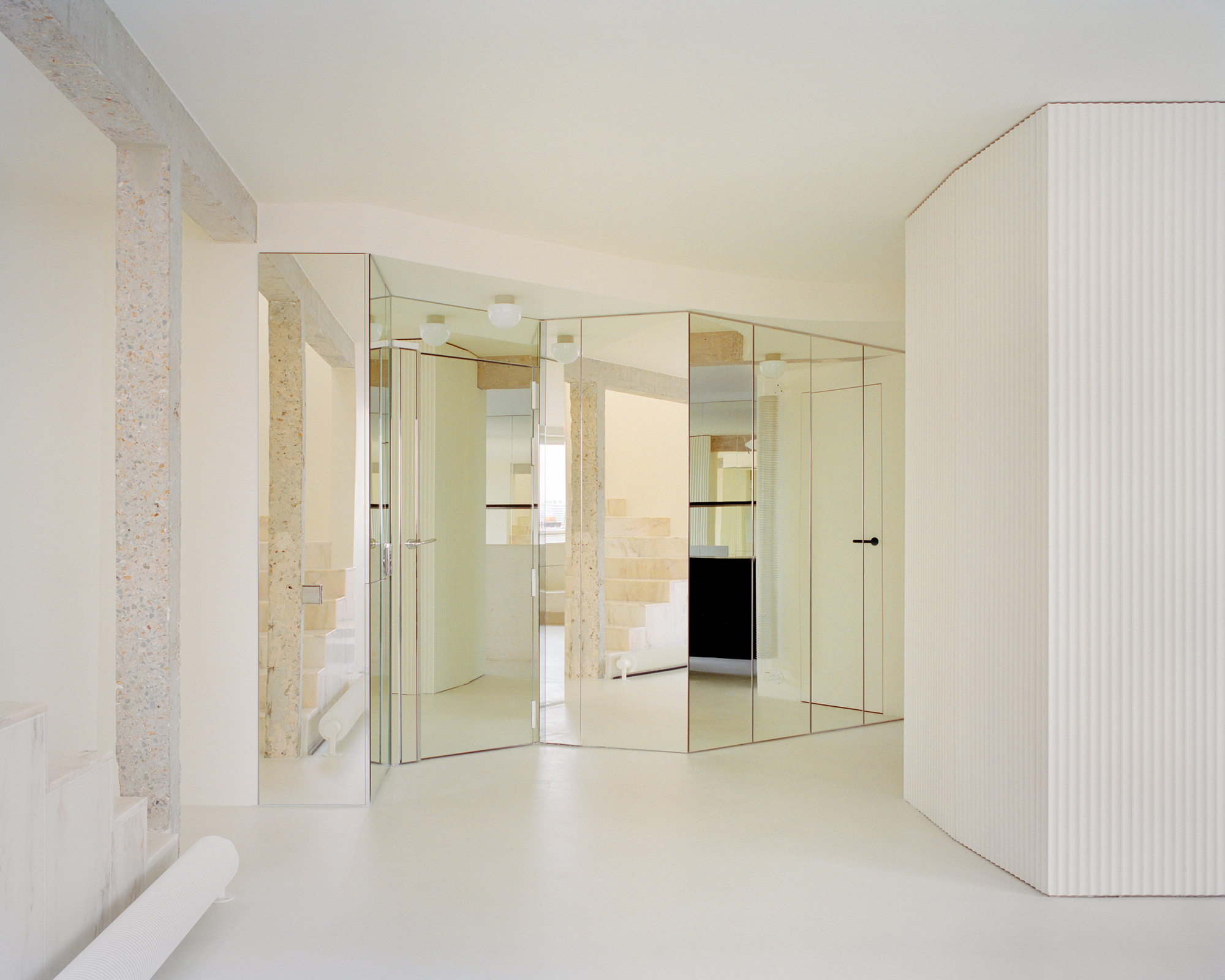 Mirrored glass partition wall reflecting the terrazzo columns and pale resin flooring