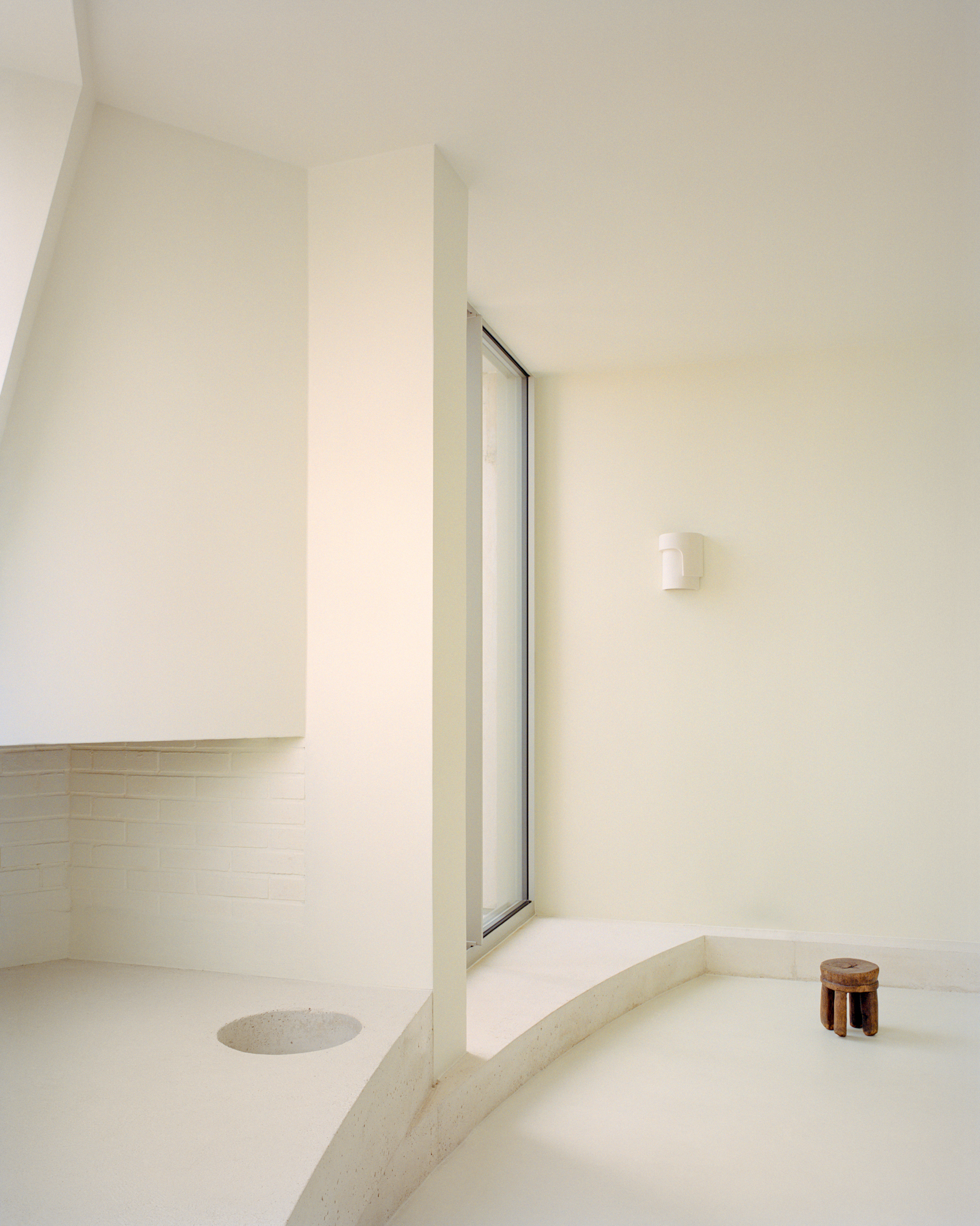 Sunken bathing area with sloped walls and a tall vertical window casting soft light
