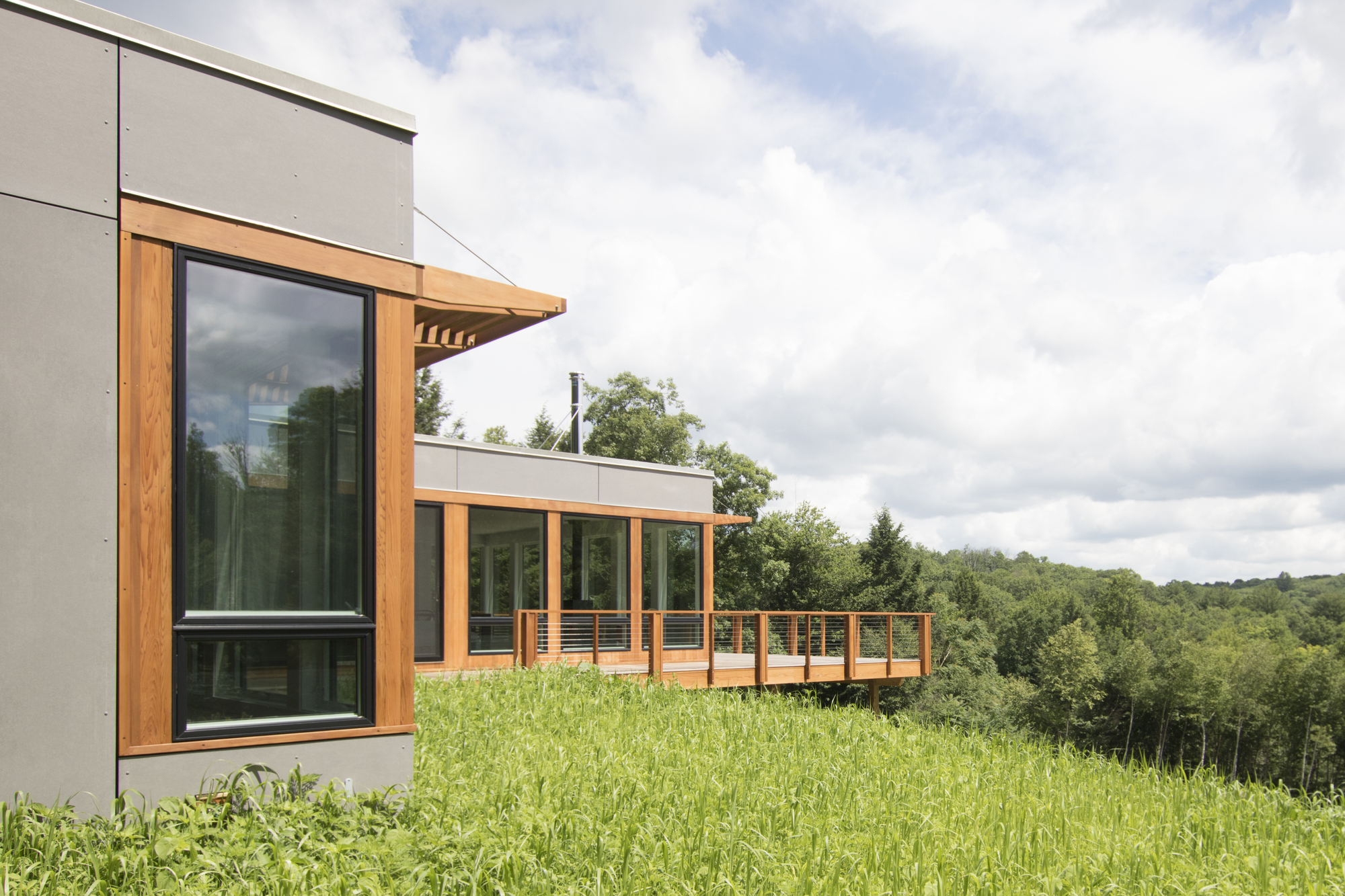 Corner detail showing timber-framed glazing and railing on a grassy slope in summer