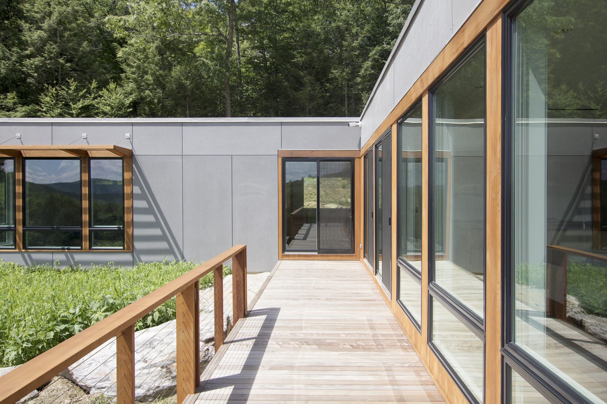 Timber boardwalk connecting glass-walled volumes with mountain views in the distance