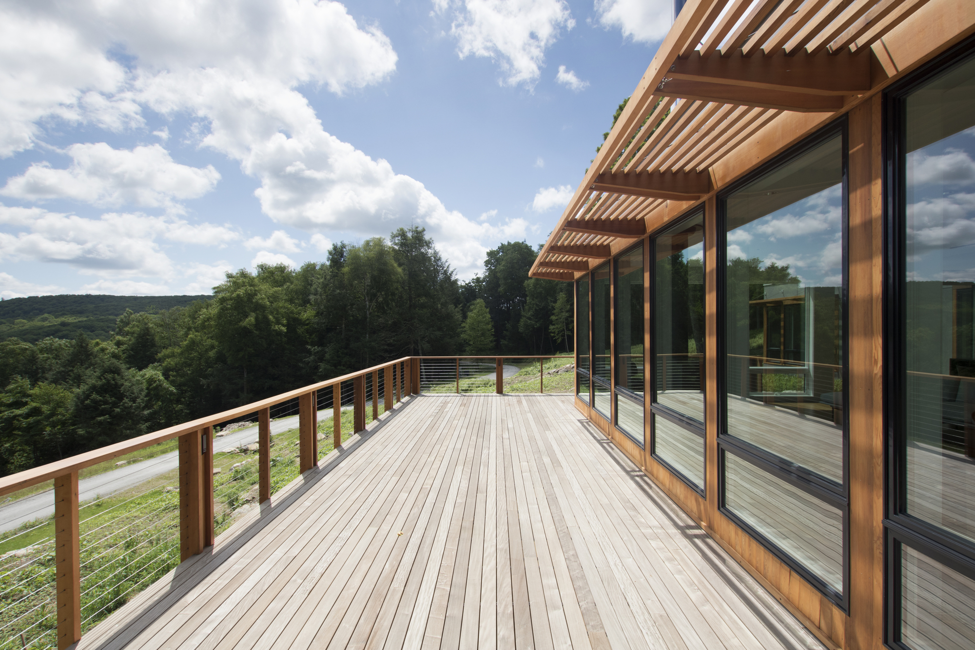 Timber deck with slatted pergola and cable railing under a blue sky with clouds