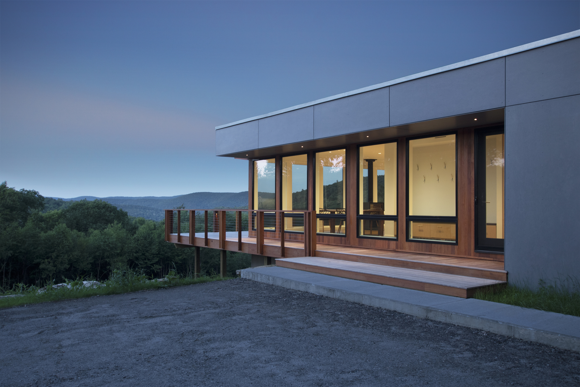 Cantilevered timber deck with vertical slat railing extending from the glazed facade at dusk