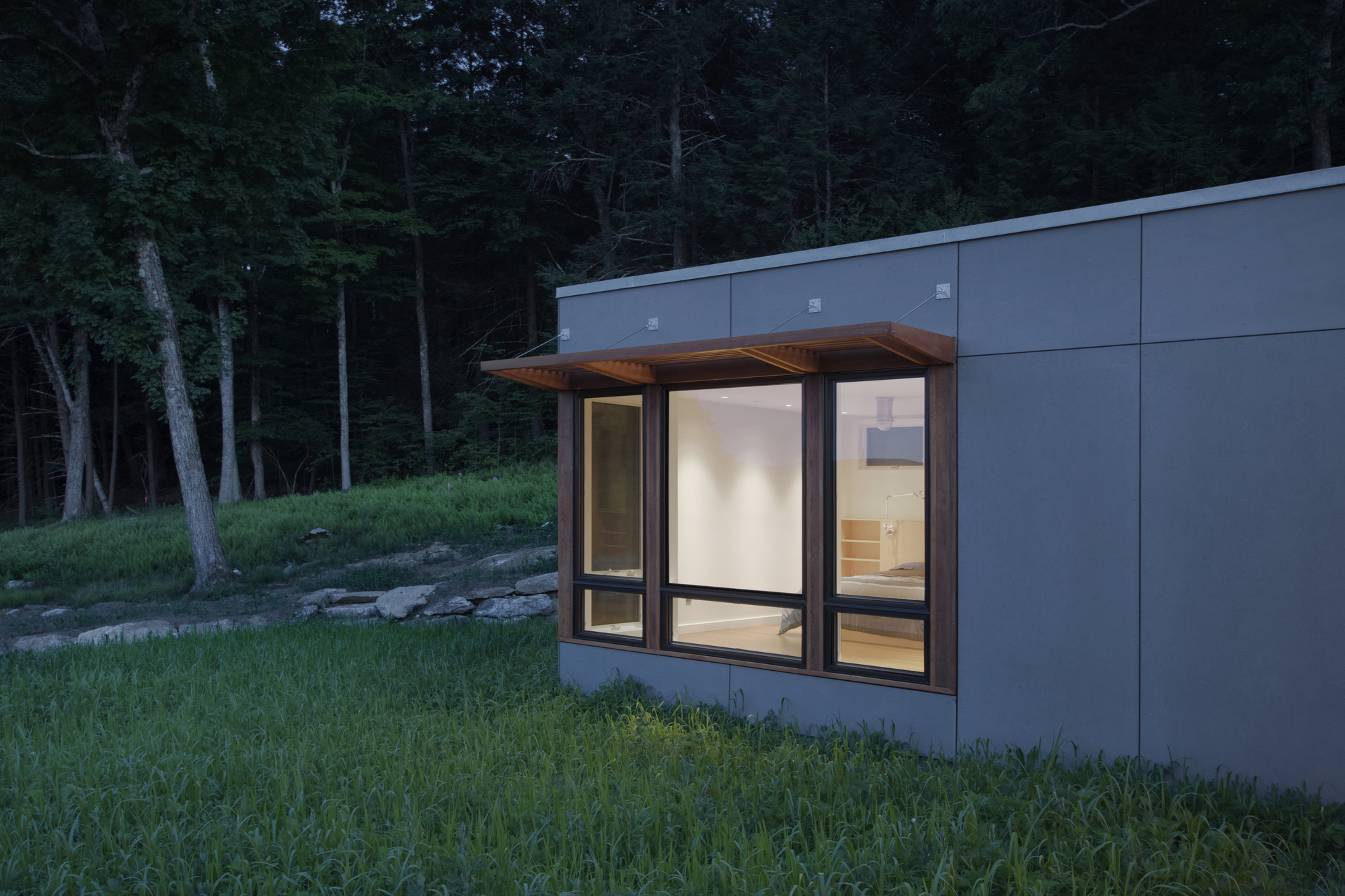 Corner bay window with timber soffit protruding from grey panel wall near wooded slope