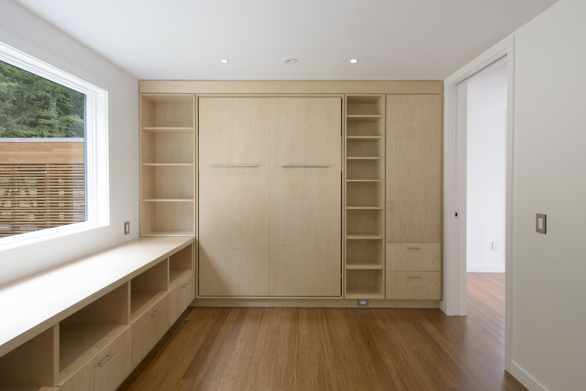 Plywood millwork wall with concealed murphy bed flanked by open shelving and window seat below deck view
