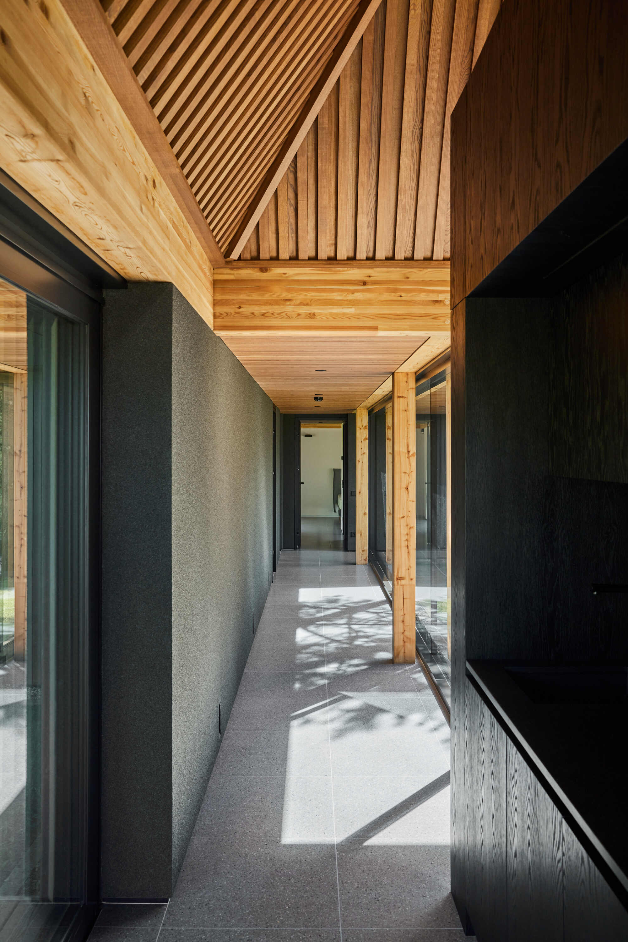 Covered walkway with exposed timber beams and slatted ceiling casting shadows on the terrazzo floor