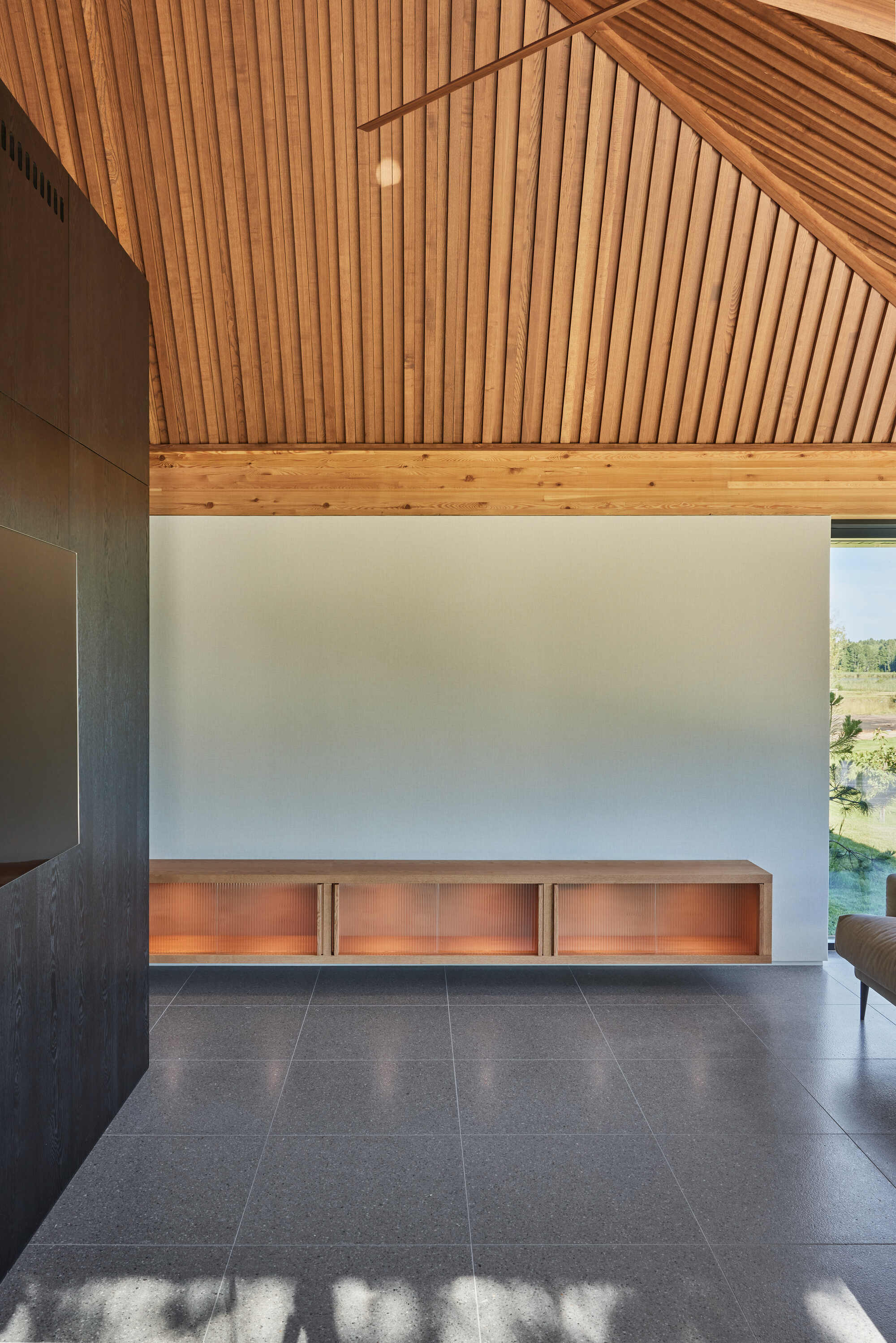 Interior with copper-lit credenza against white wall beneath angled timber slat ceiling and afternoon sun