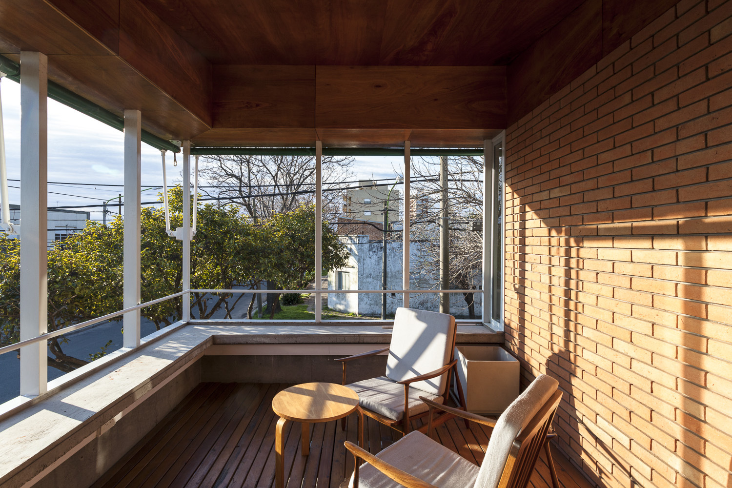 Upper-level timber-lined terrace with white steel columns, wood decking and views to neighboring rooftops in afternoon light